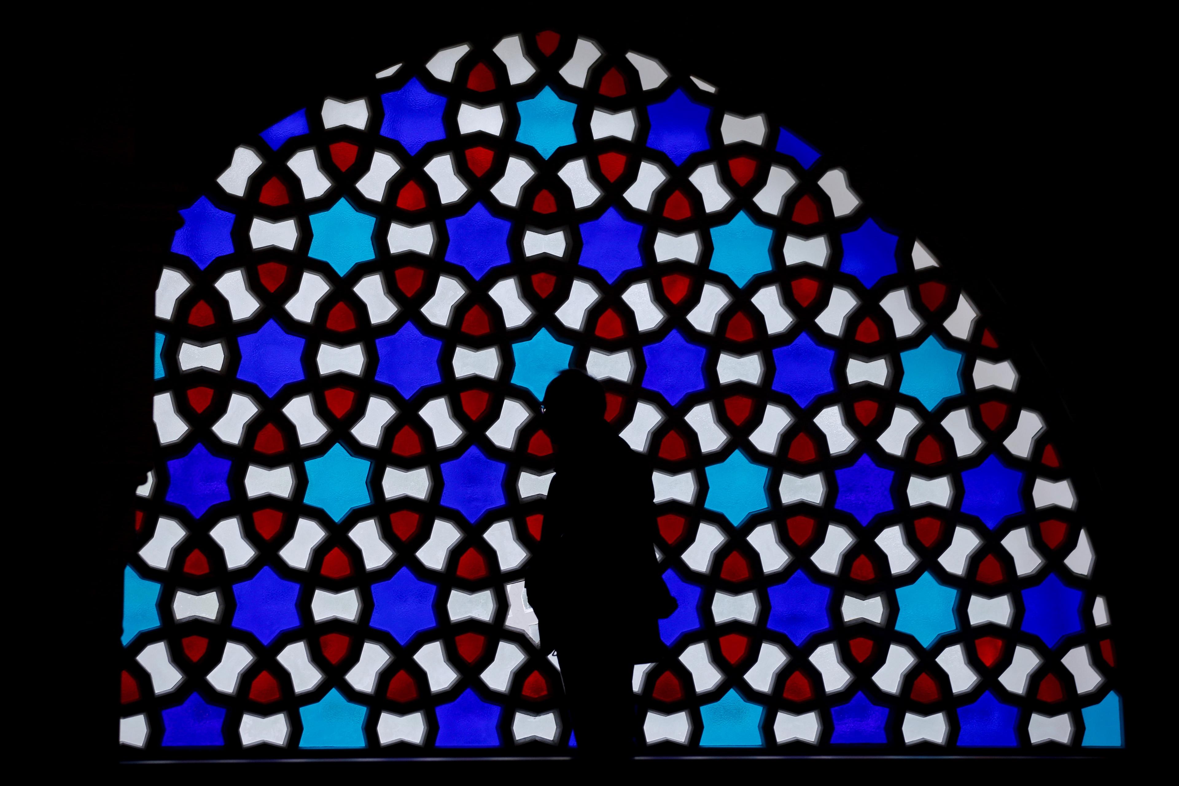 Silhouette of person against a colourful stained glass window with geometric patterns in a photo.