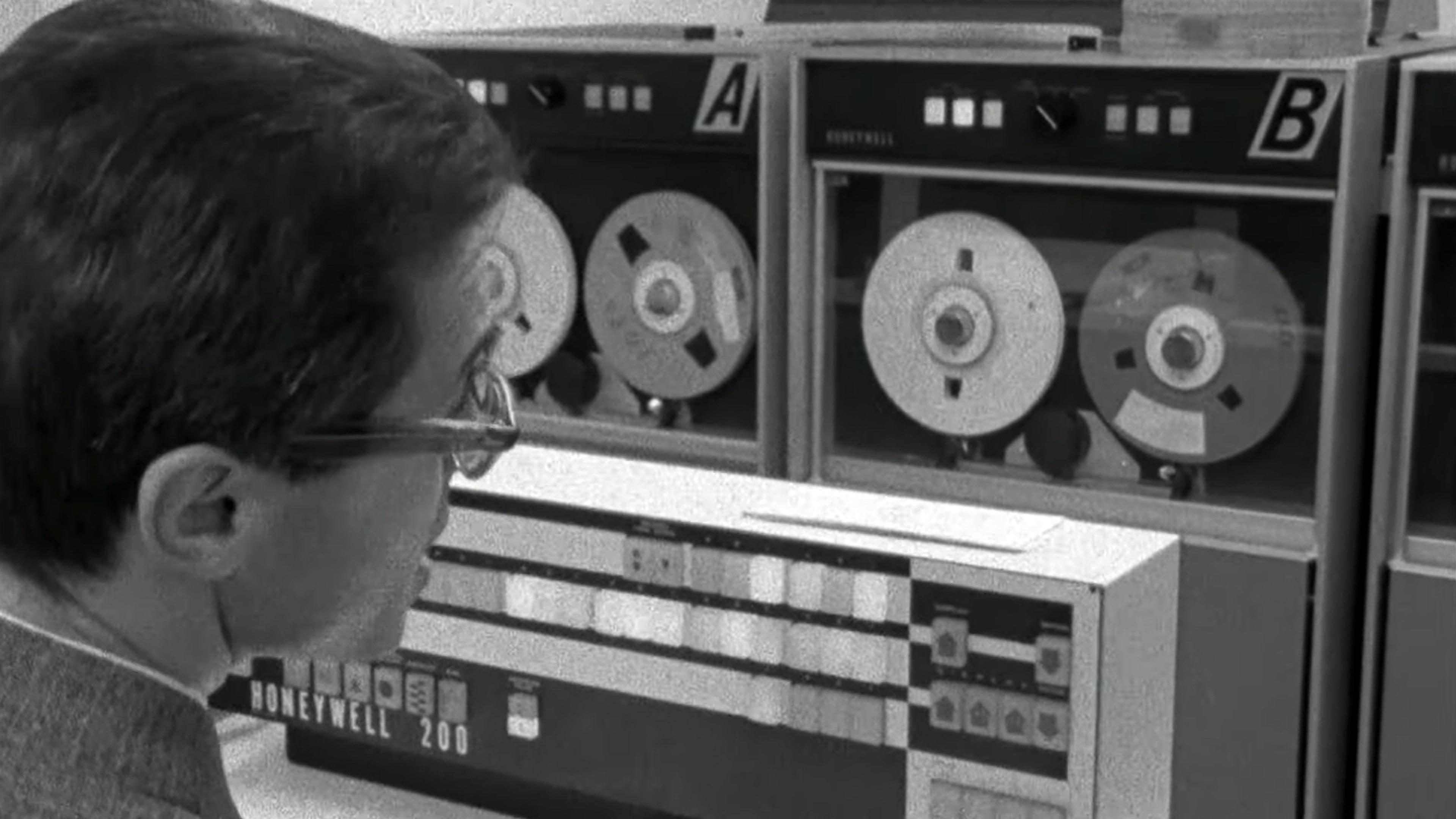 Black-and-white photo of a person looking at vintage Honeywell 200 computer tape drives labelled A and B.