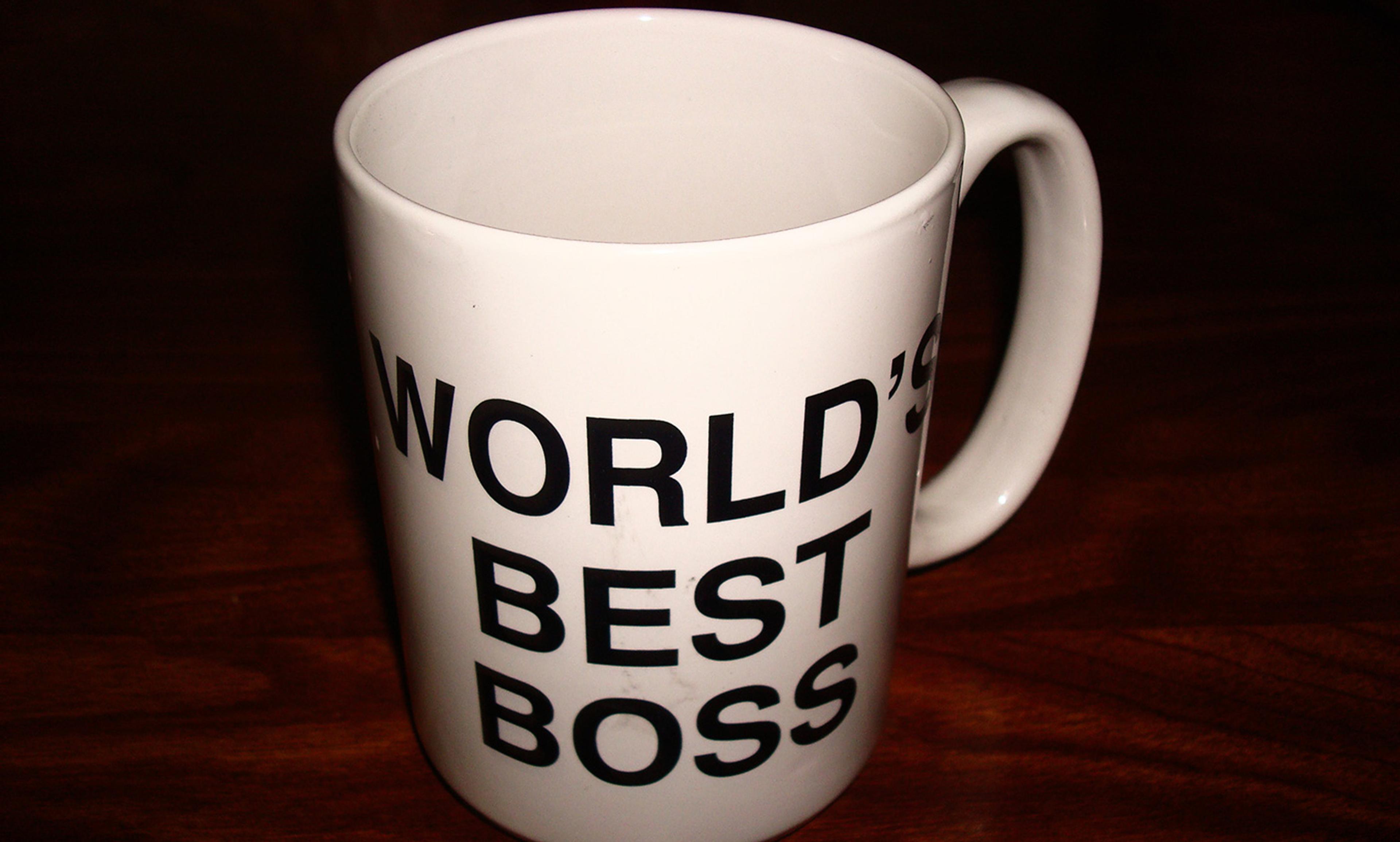 A white mug with black text reading “WORLD’S BEST BOSS,” placed on a dark wooden surface.