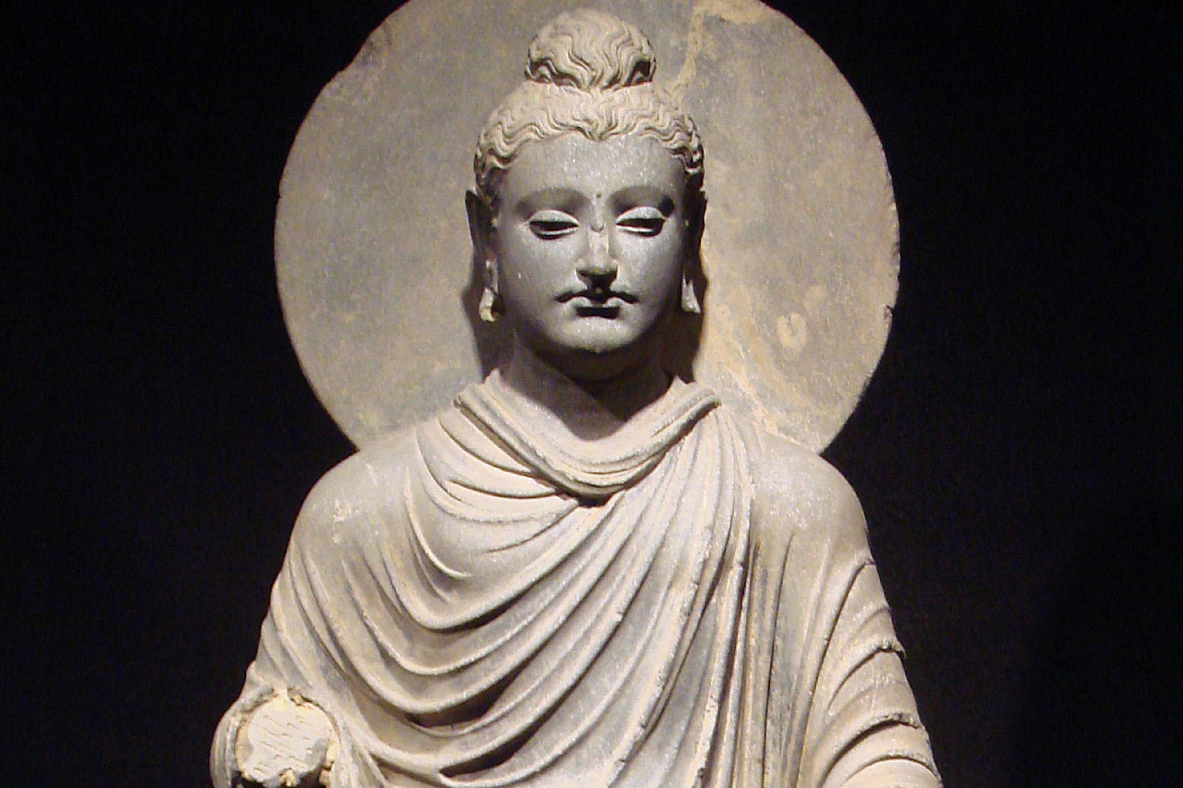 Stone sculpture of a serene figure in draped robes with a halo against a dark background.