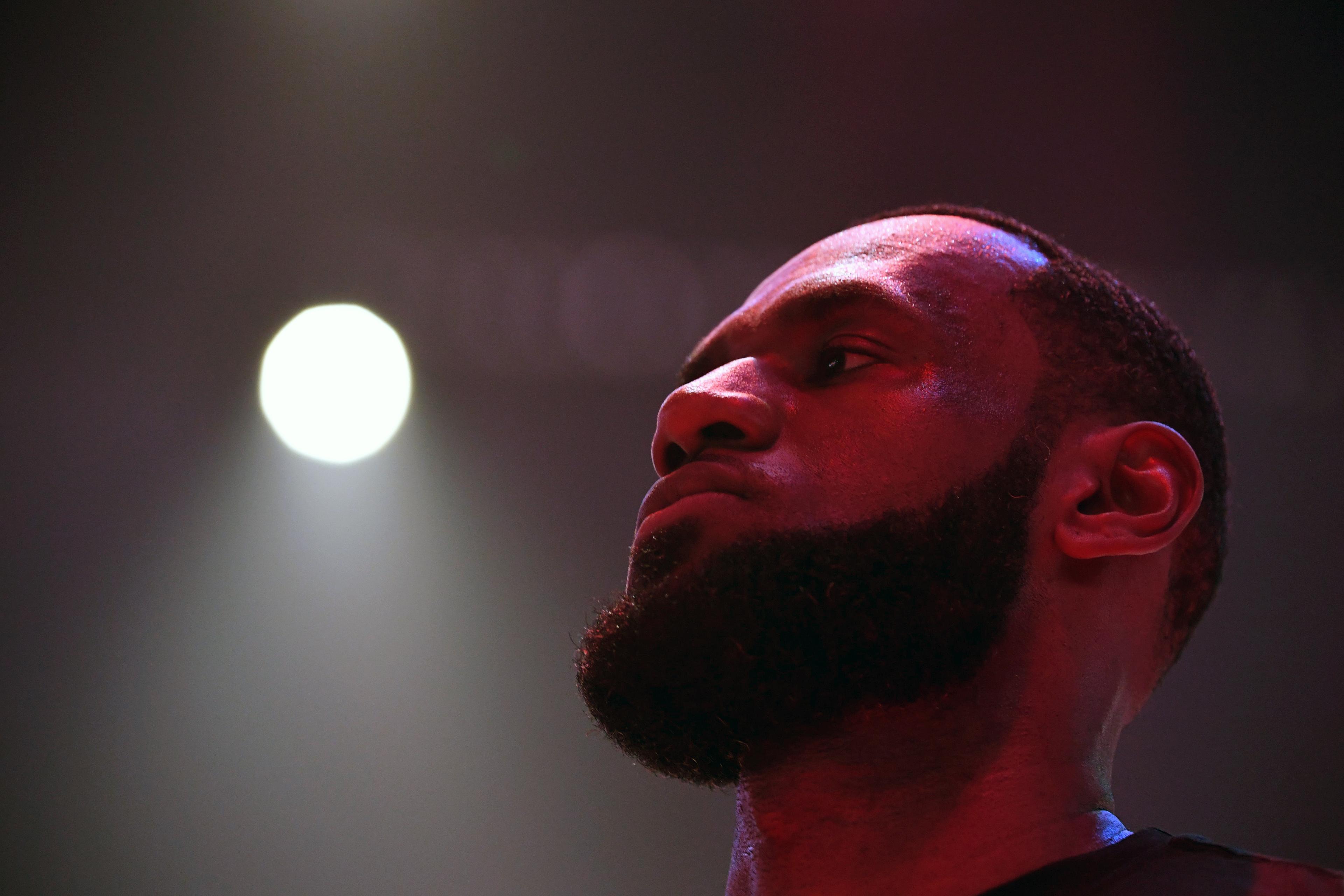 Photo of a bearded man with a strong jawline in low red lighting, bright spotlight in background.