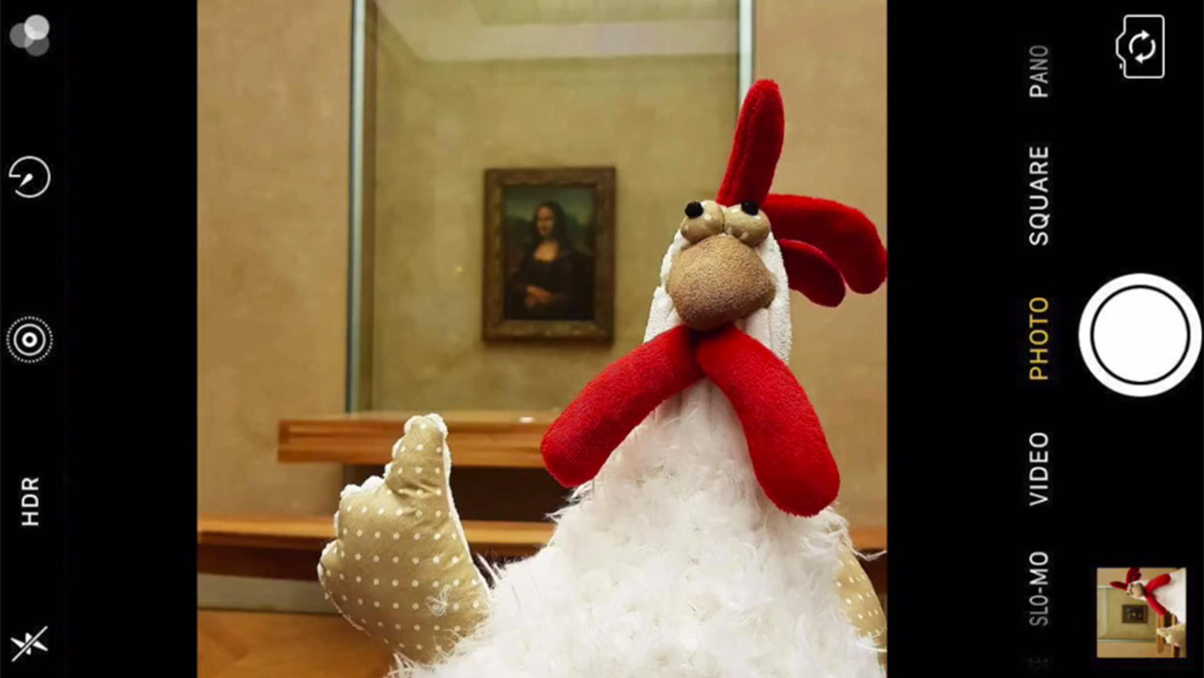 A toy chicken in front of the Mona Lisa painting, viewed through a smartphone camera interface.