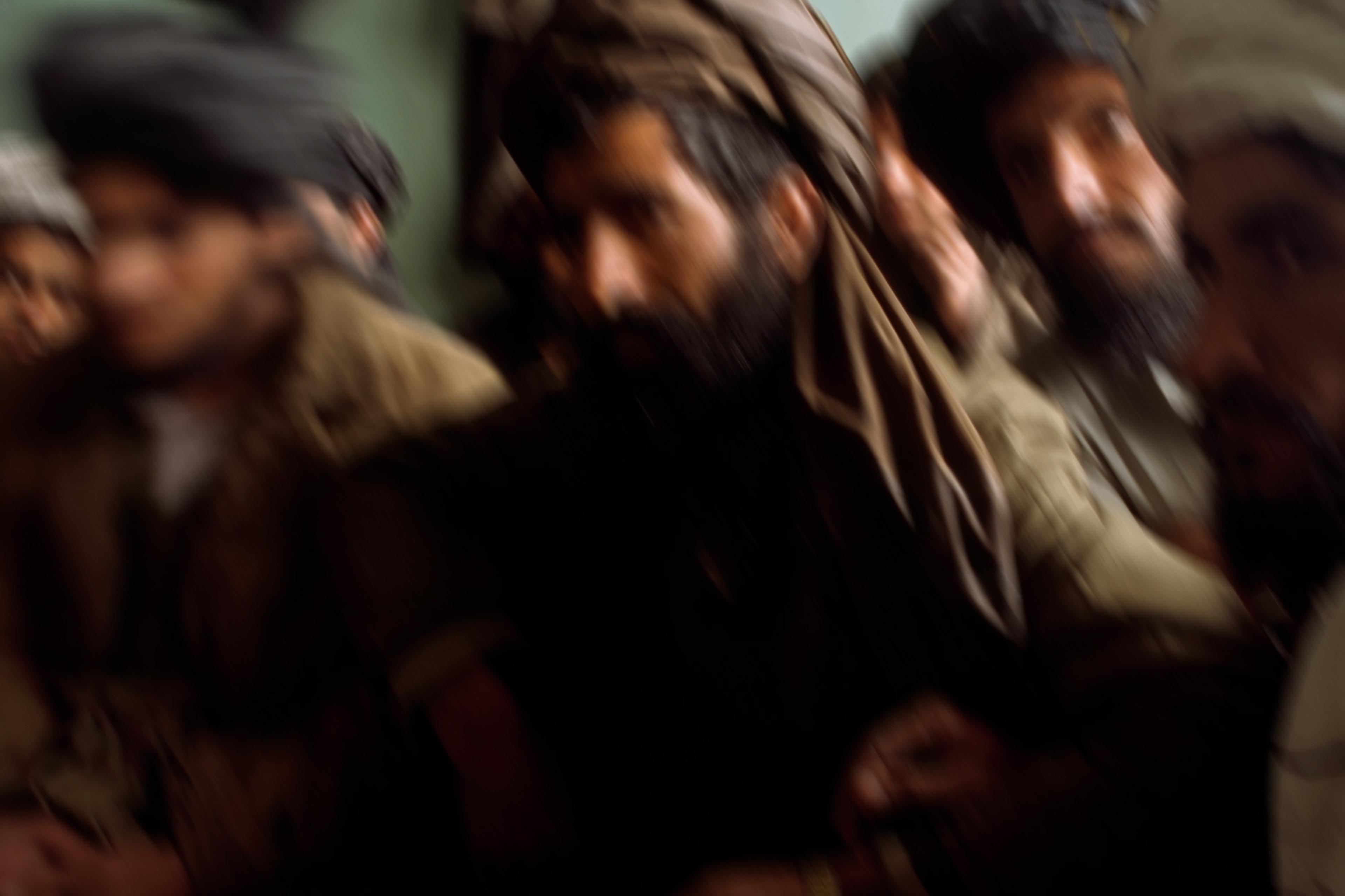 Blurry photo of a group of men wearing turbans in dim lighting against a green wall.