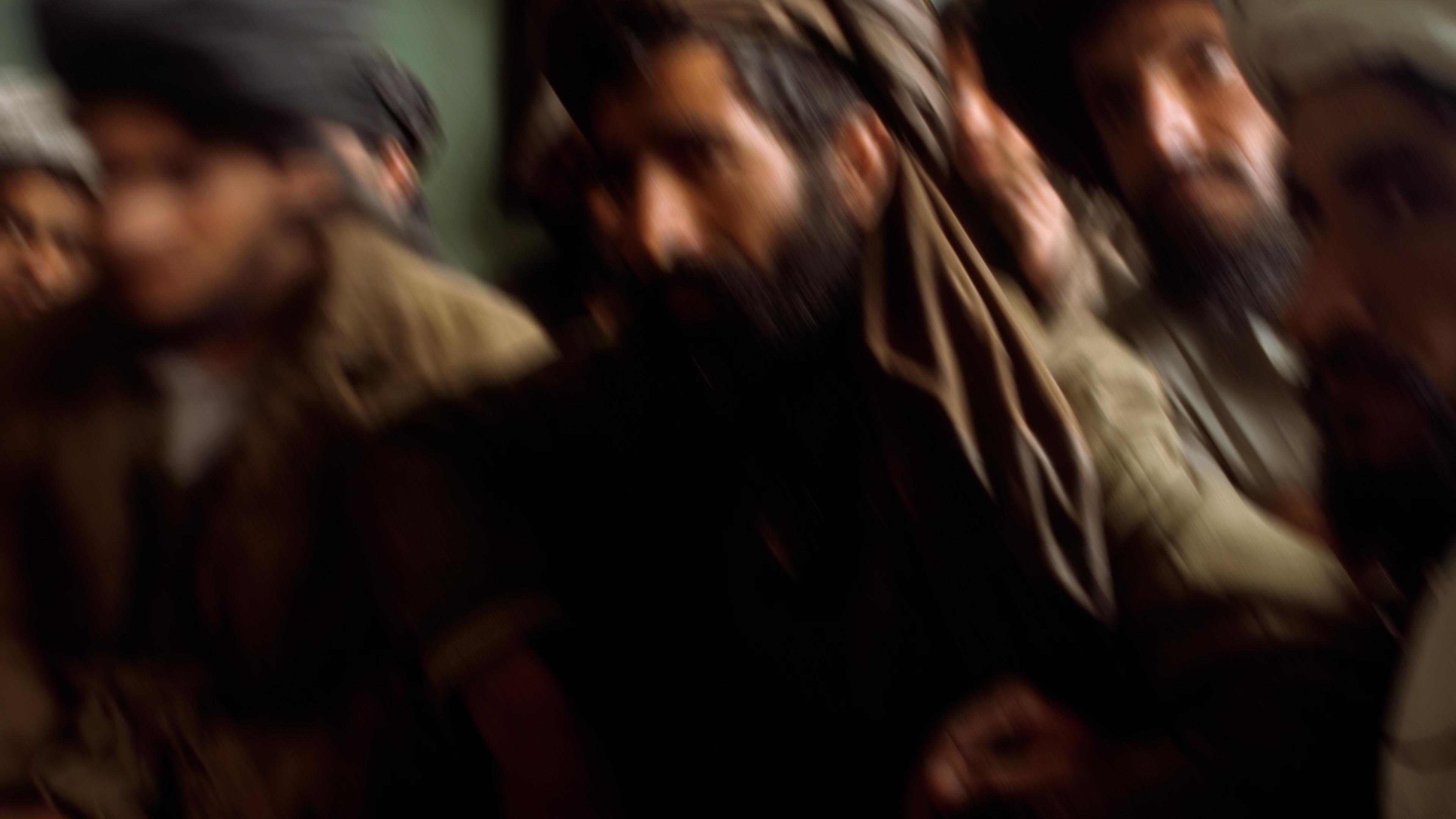Blurry photo of a group of men wearing turbans in dim lighting against a green wall.