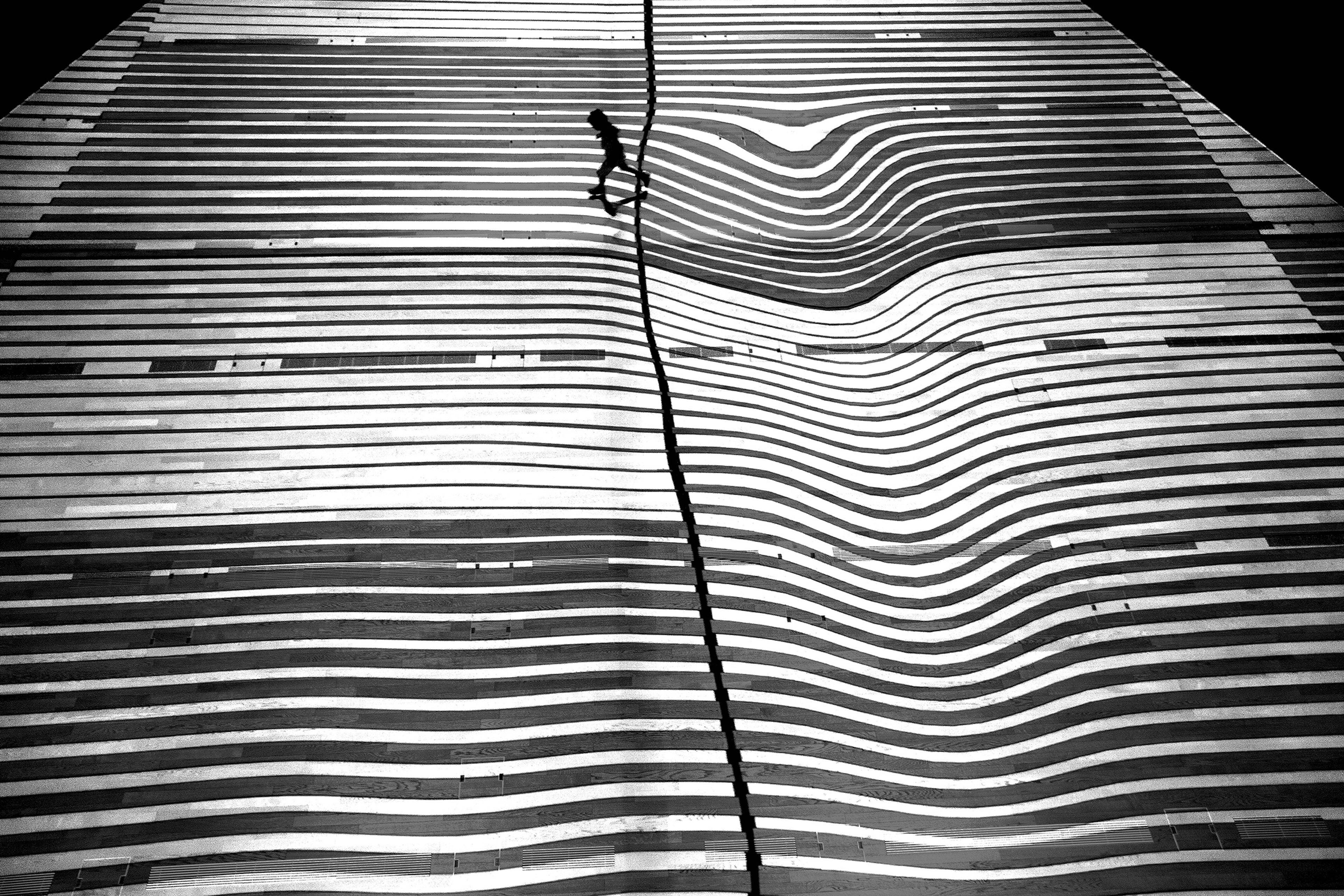 Black and white photo of a person walking on a wavy striped surface creating an optical illusion.