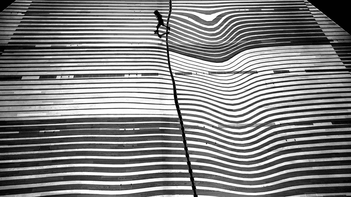 Black and white photo of a person walking on a wavy striped surface creating an optical illusion.