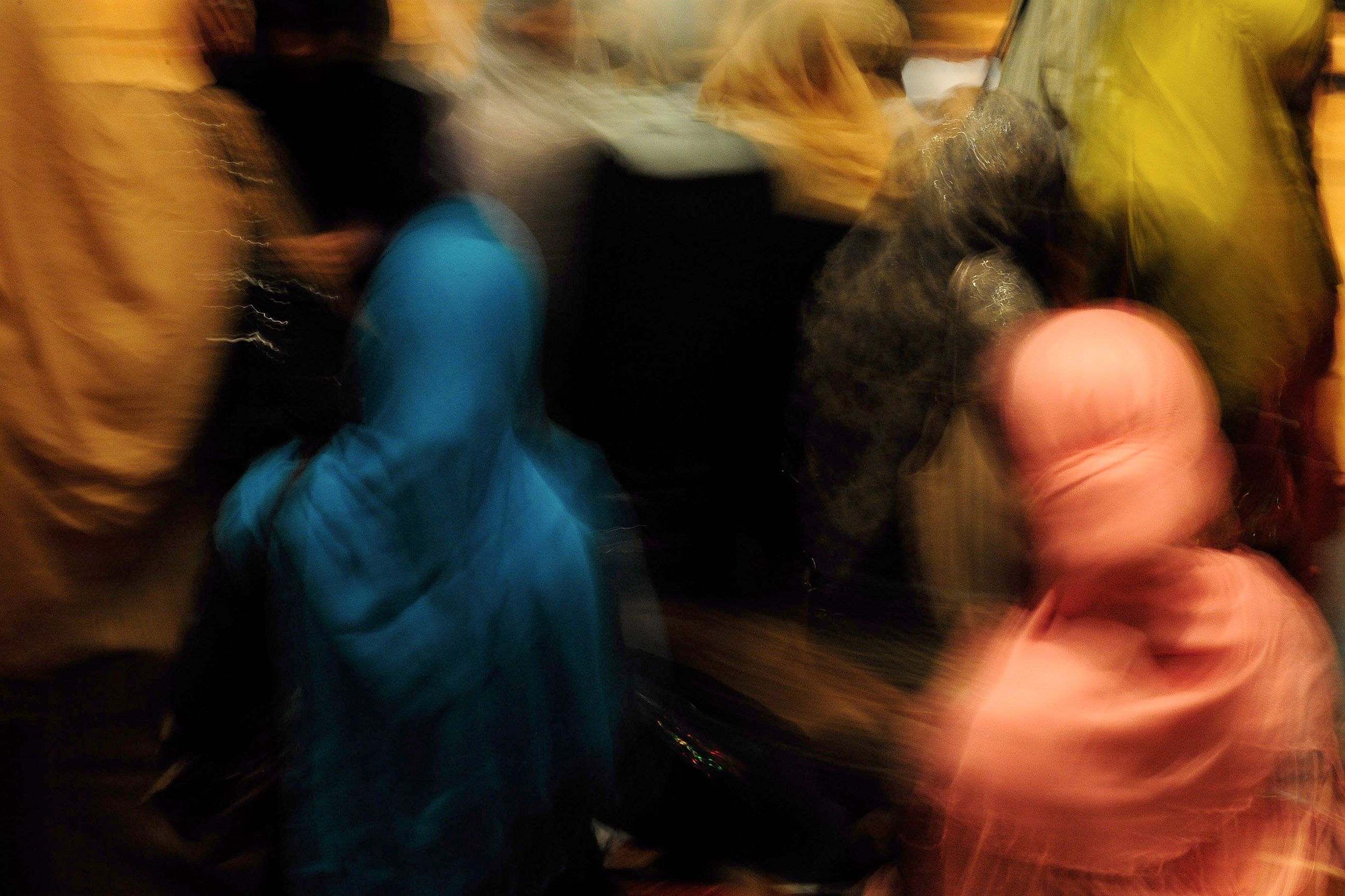 Abstract photo of people blurred in motion wearing colourful hijabs; colours include blue, pink and yellow.