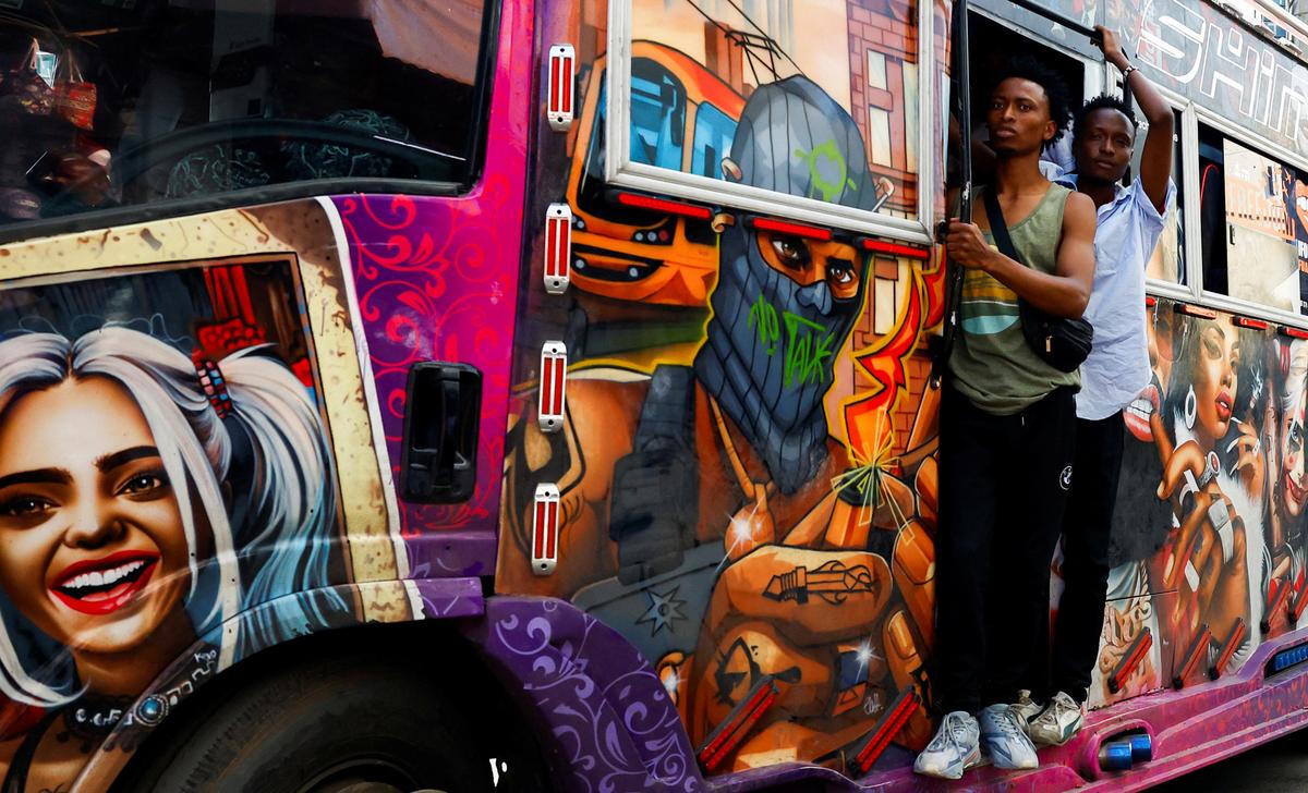 A colourful graffiti-covered bus with two men standing in the doorway, featuring vibrant character artwork.