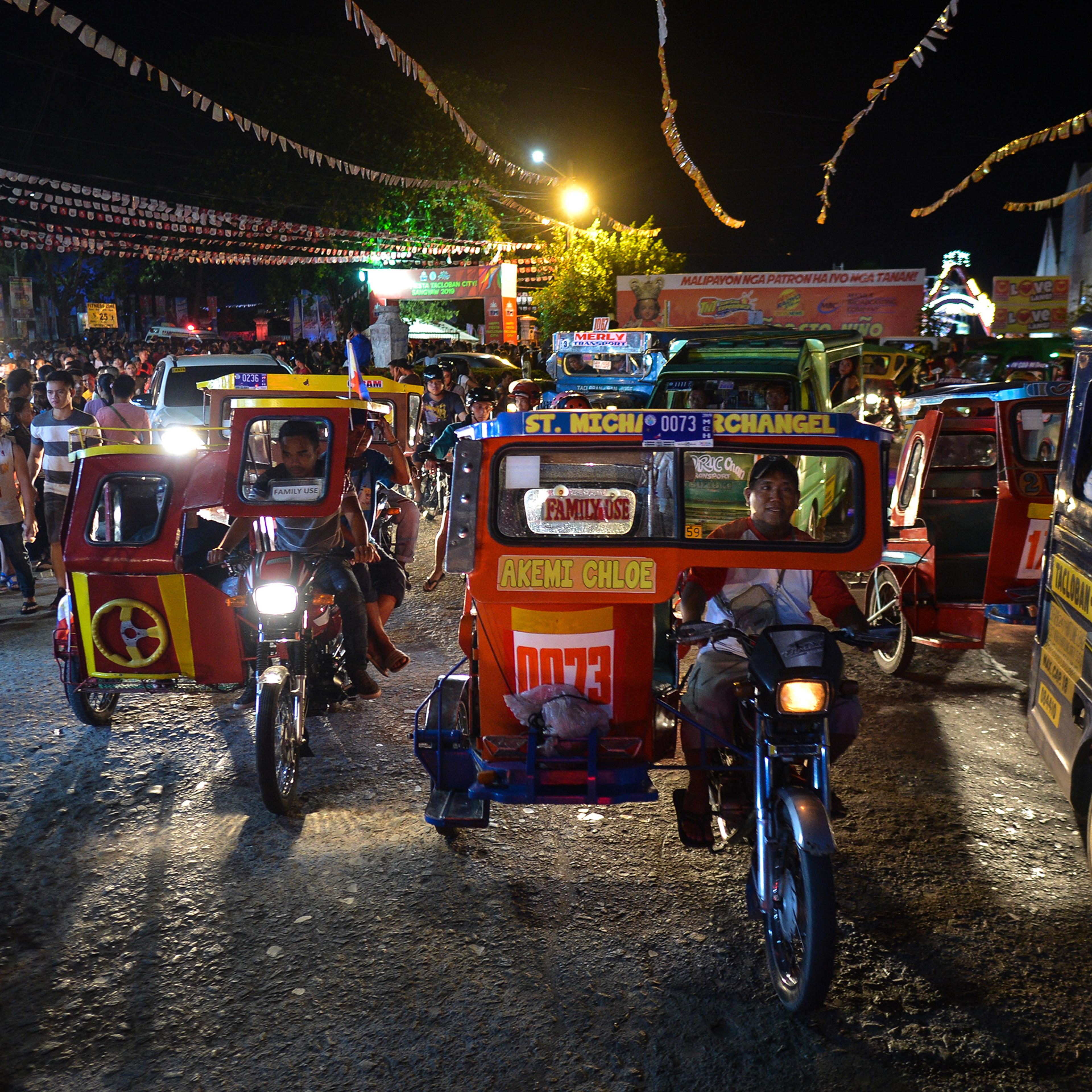 Photo of a busy night street market with people and colourful tricycles in the Philippines, lit by street lights and signage.