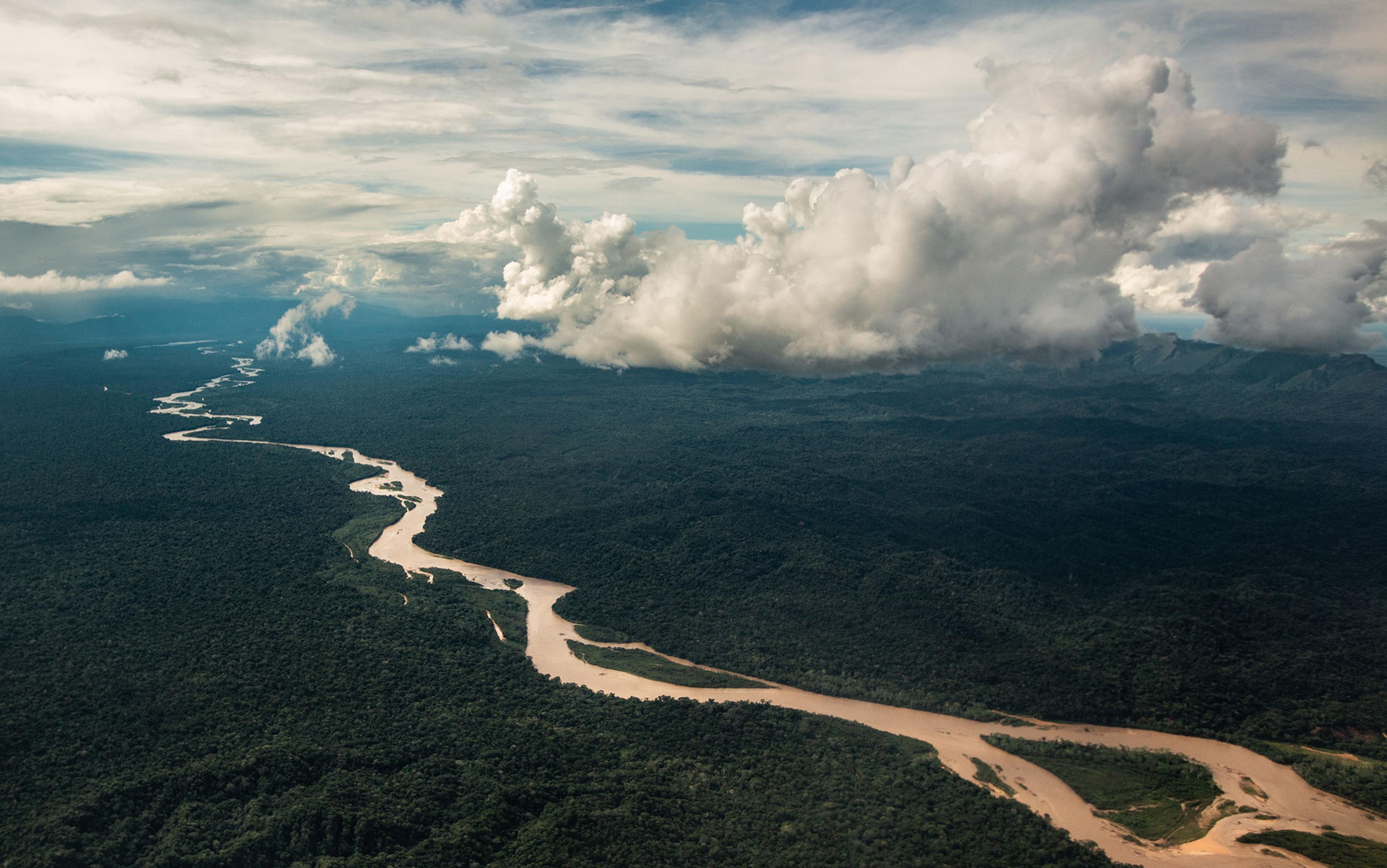 Aerial photo of a winding river through lush green rainforest with dramatic cloud formations in the sky above.