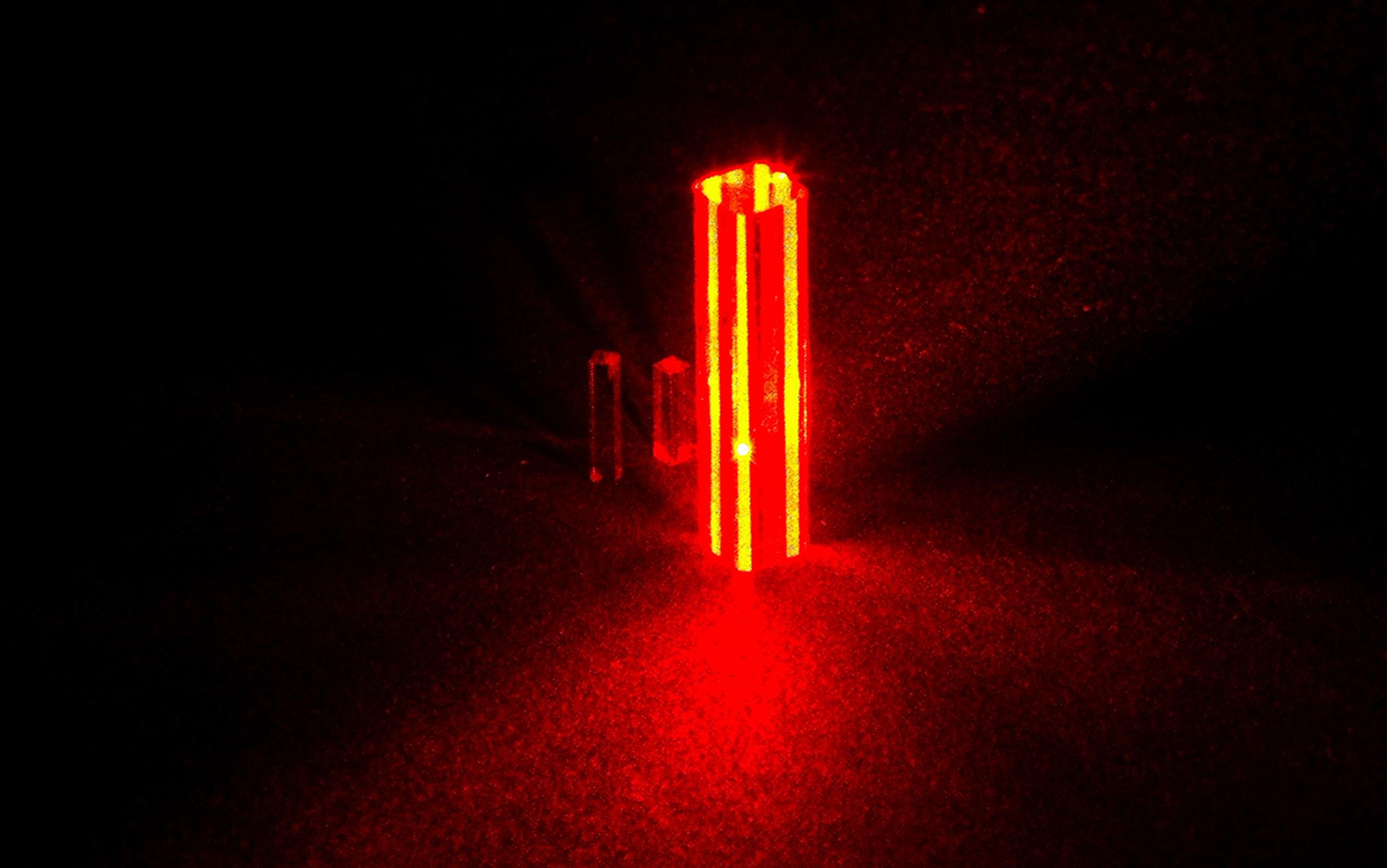 Photo of three vertical beams of red laser light in a dark room creating a glowing effect on the floor.