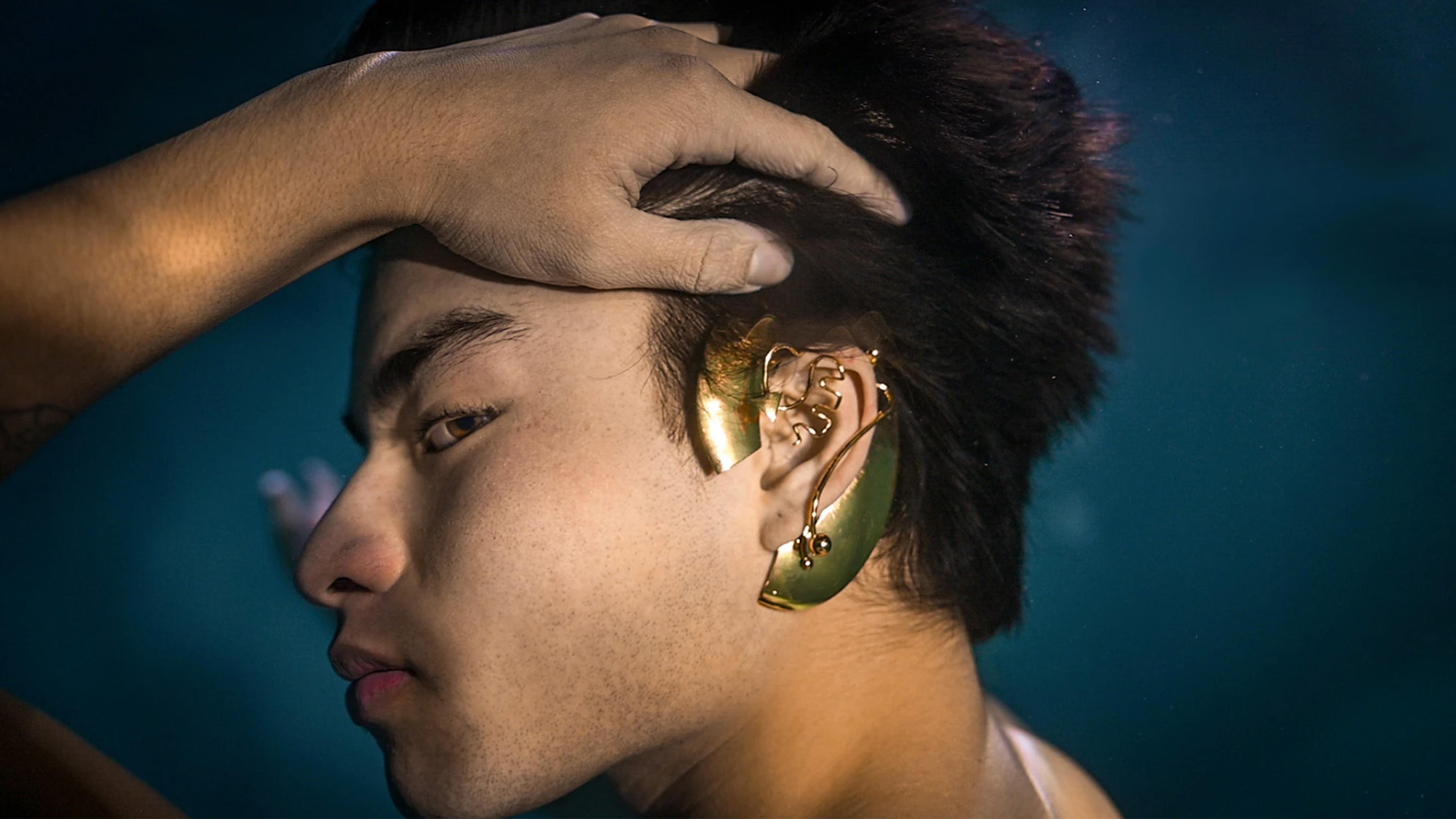 A young man turns his head with his hand to reveal a unique gold ear accessory.