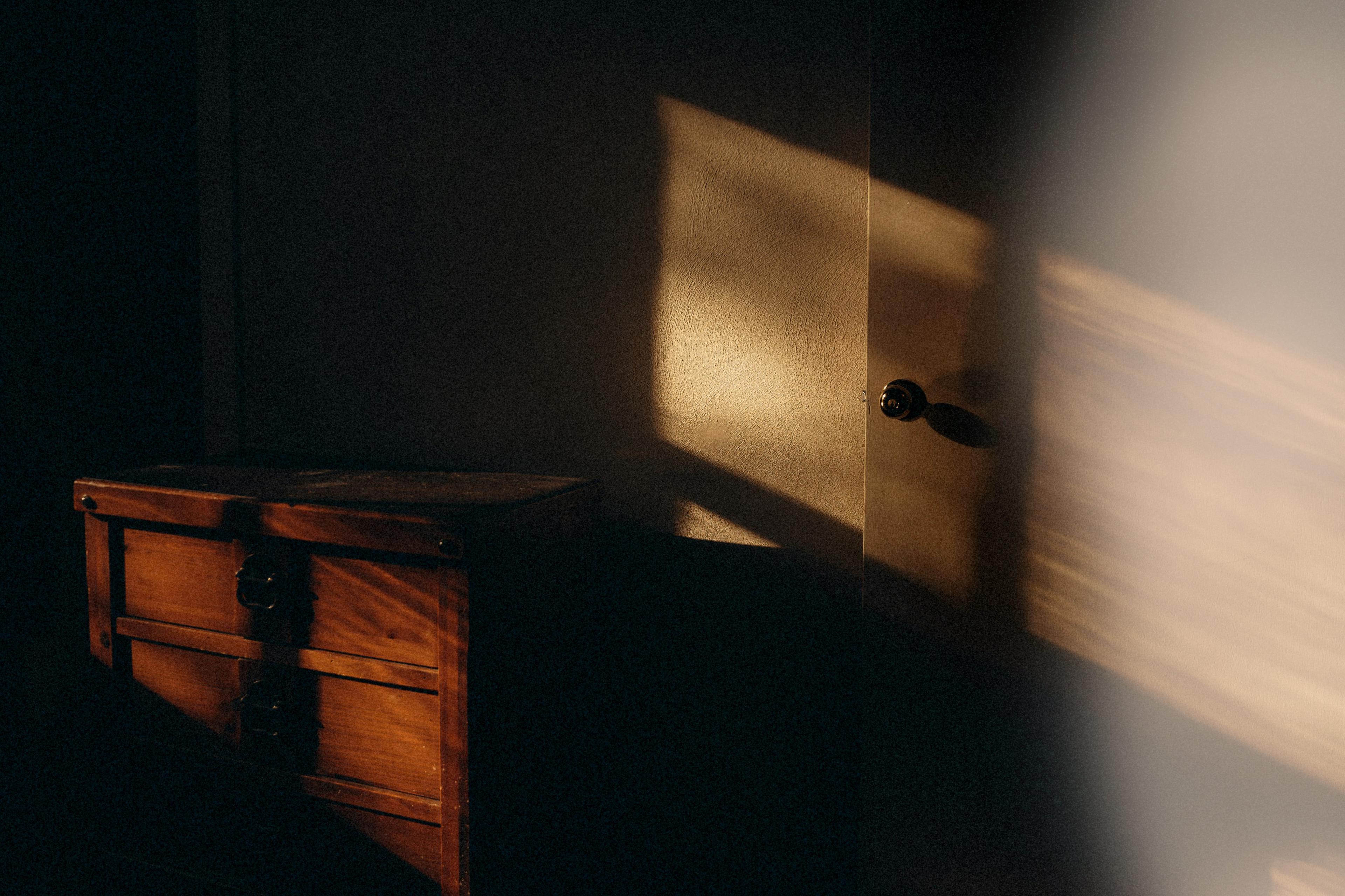 Warm sunlight casting shadows on a wooden chest and a door inside a dimly lit room.