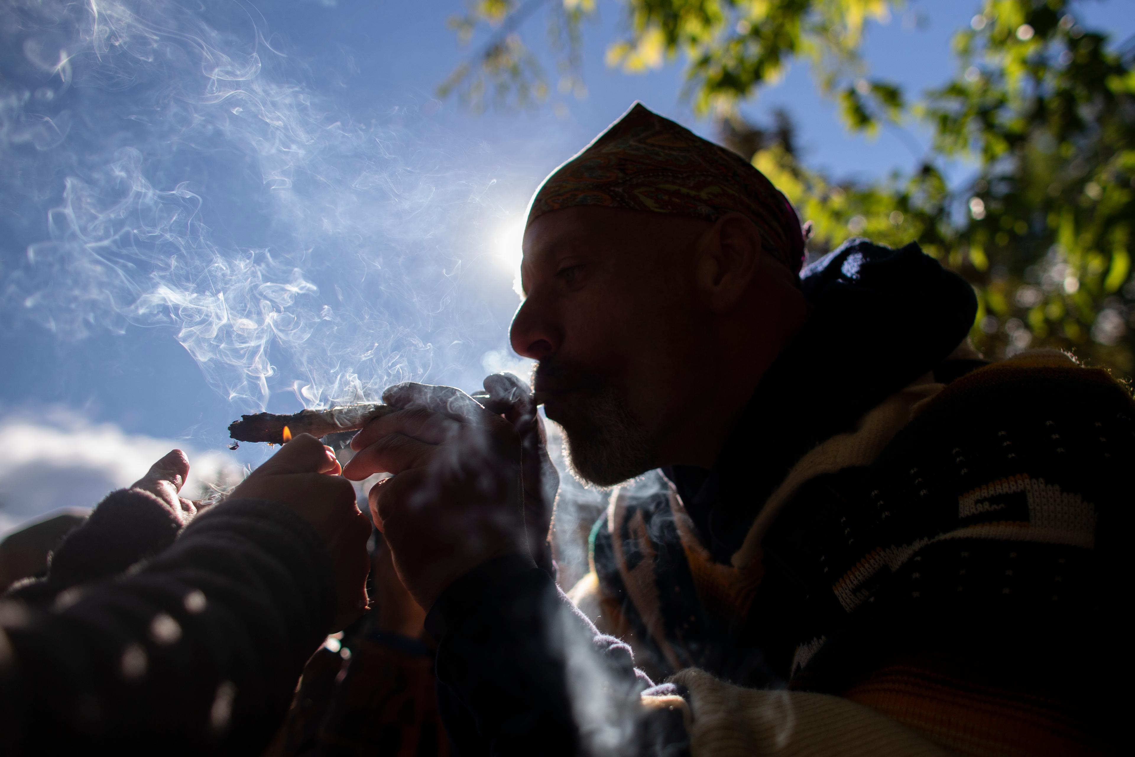 Photo of a person outdoors smoking, silhouetted against the sky with visible smoke and surrounding greenery.