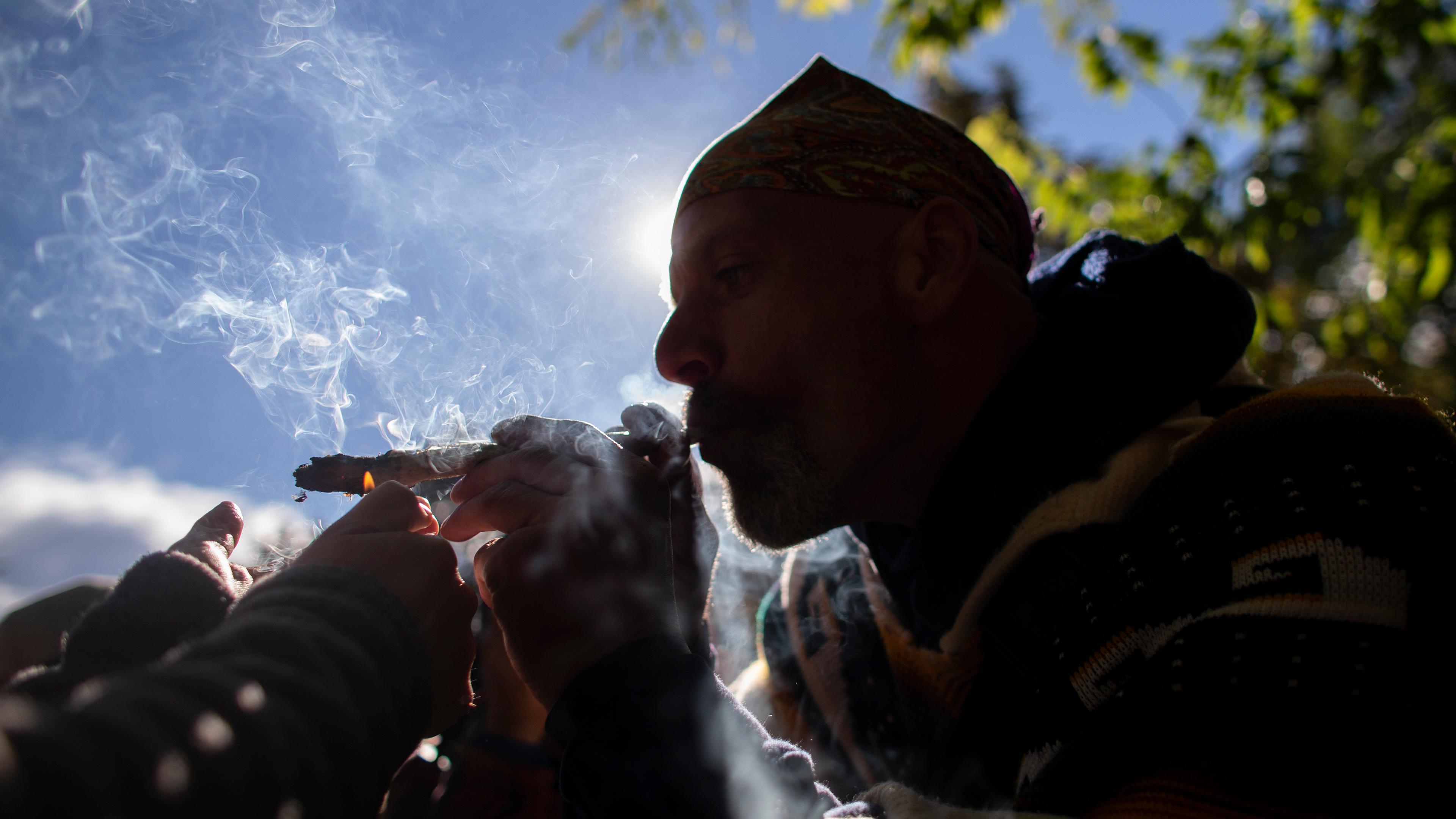 Photo of a person outdoors smoking, silhouetted against the sky with visible smoke and surrounding greenery.