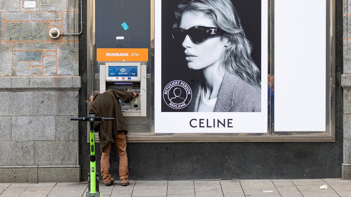 A person using a Minibank ATM next to a Celine advert with an electric scooter parked nearby.