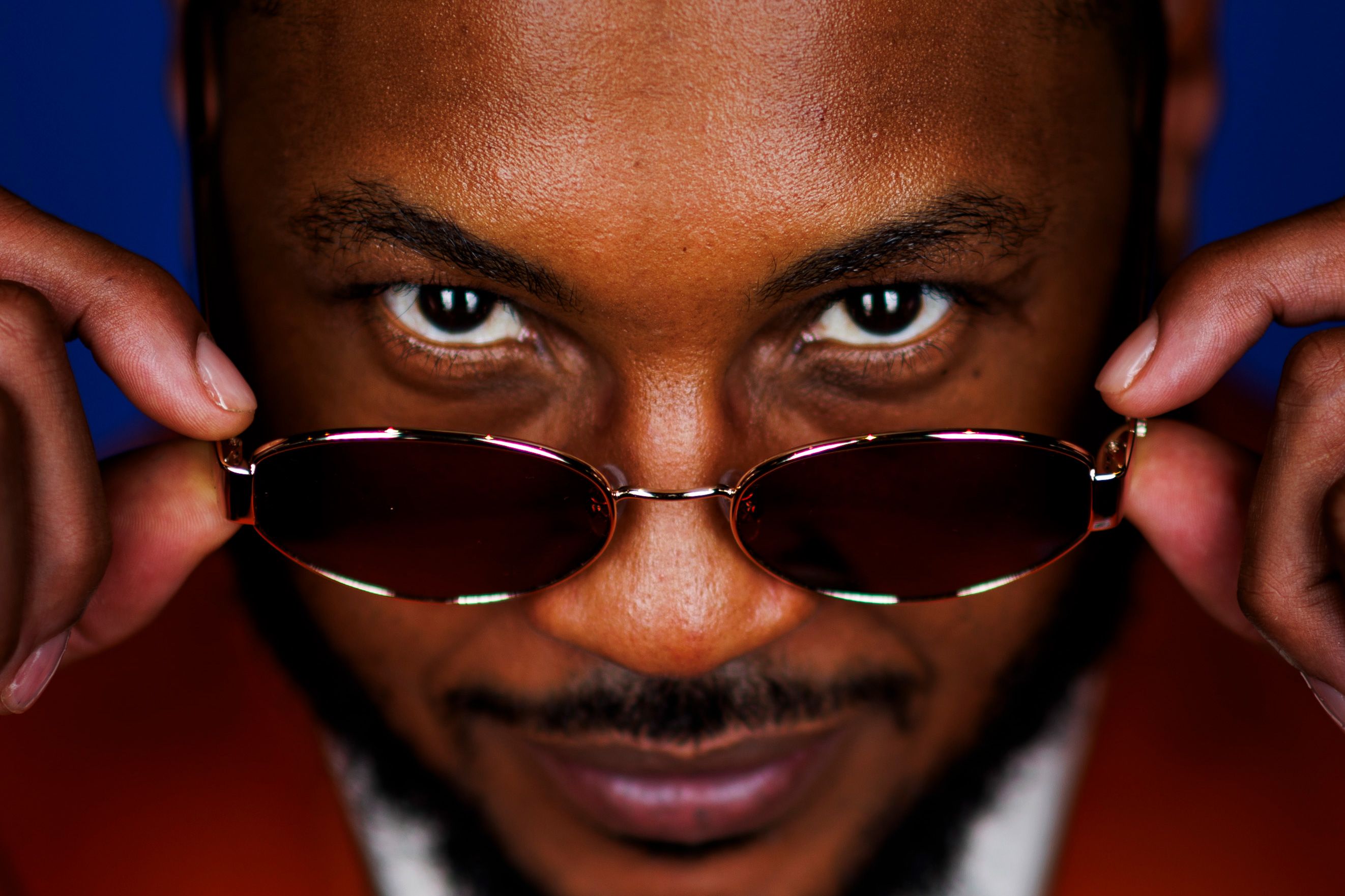 Photo of a man with sunglasses lowered, gazing directly at the camera with a smile against a blue background.