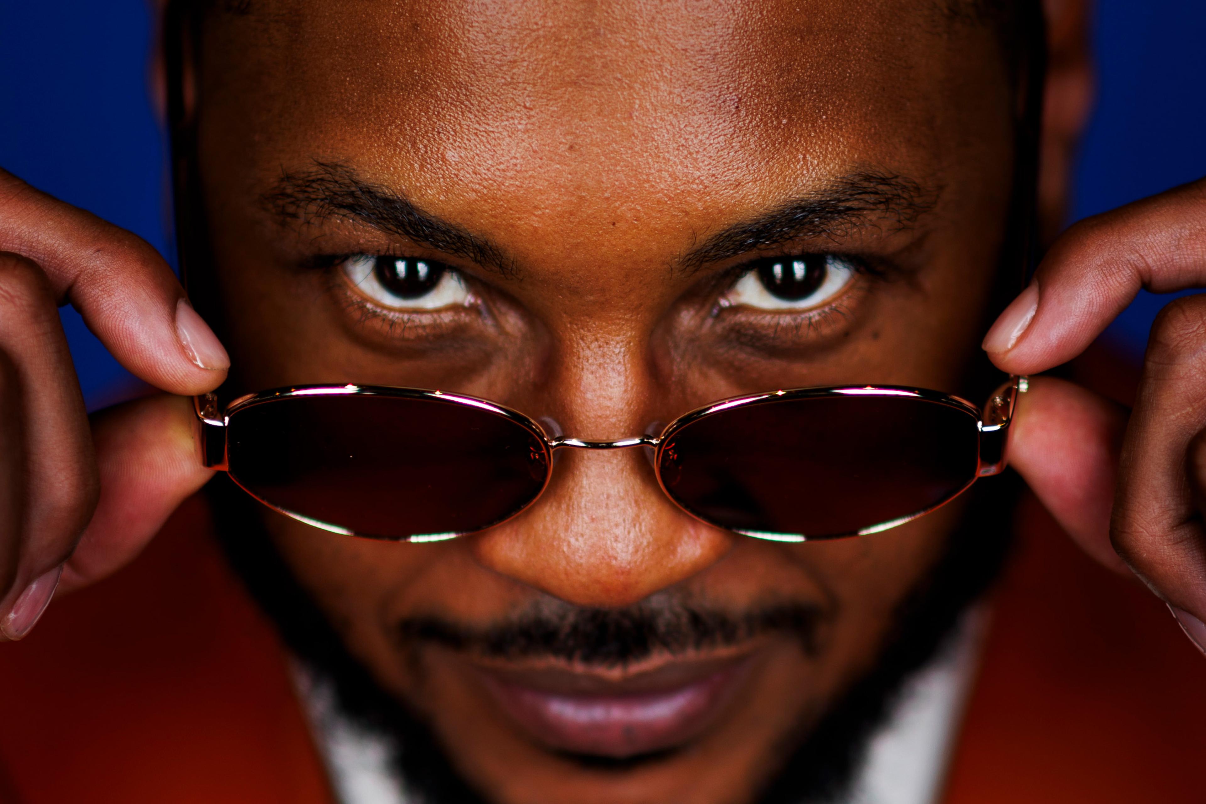 Photo of a man with sunglasses lowered, gazing directly at the camera with a smile against a blue background.