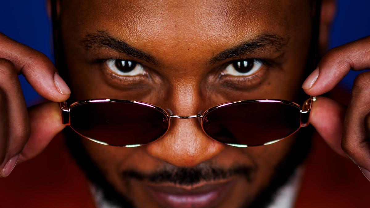 Photo of a man with sunglasses lowered, gazing directly at the camera with a smile against a blue background.