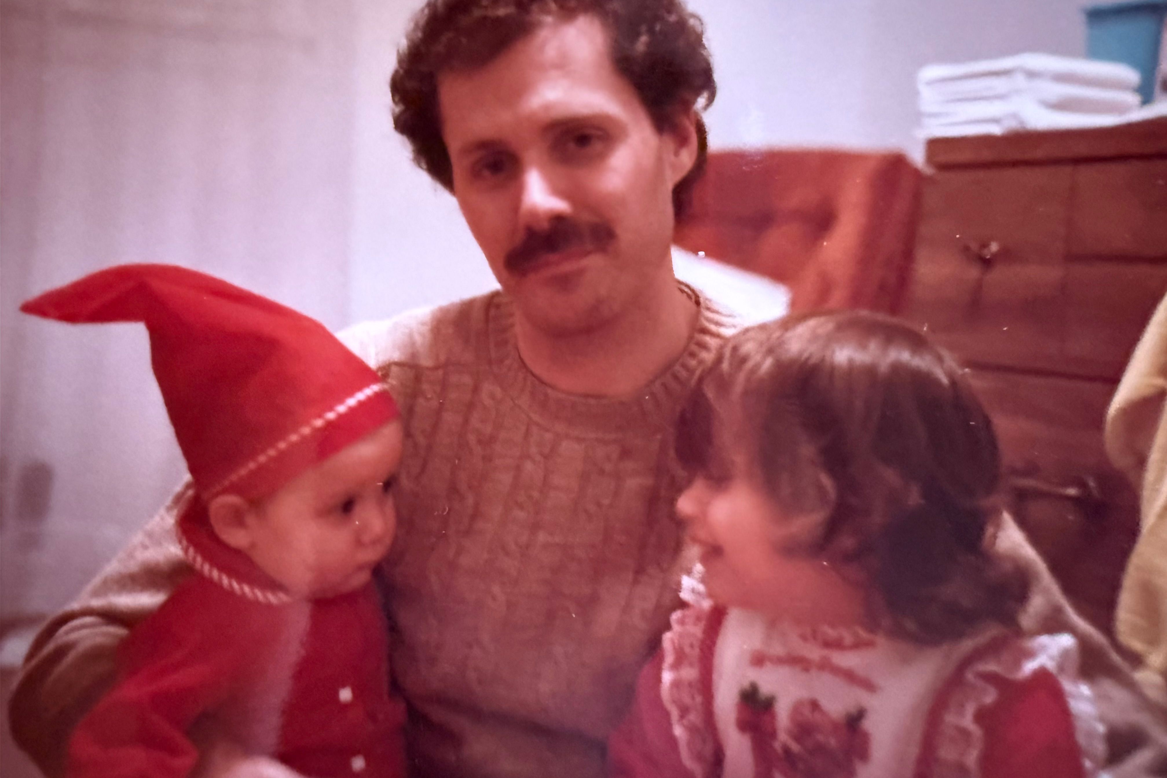 Vintage photo of a man with a moustache holding a baby wearing a red pointed cap and a young child