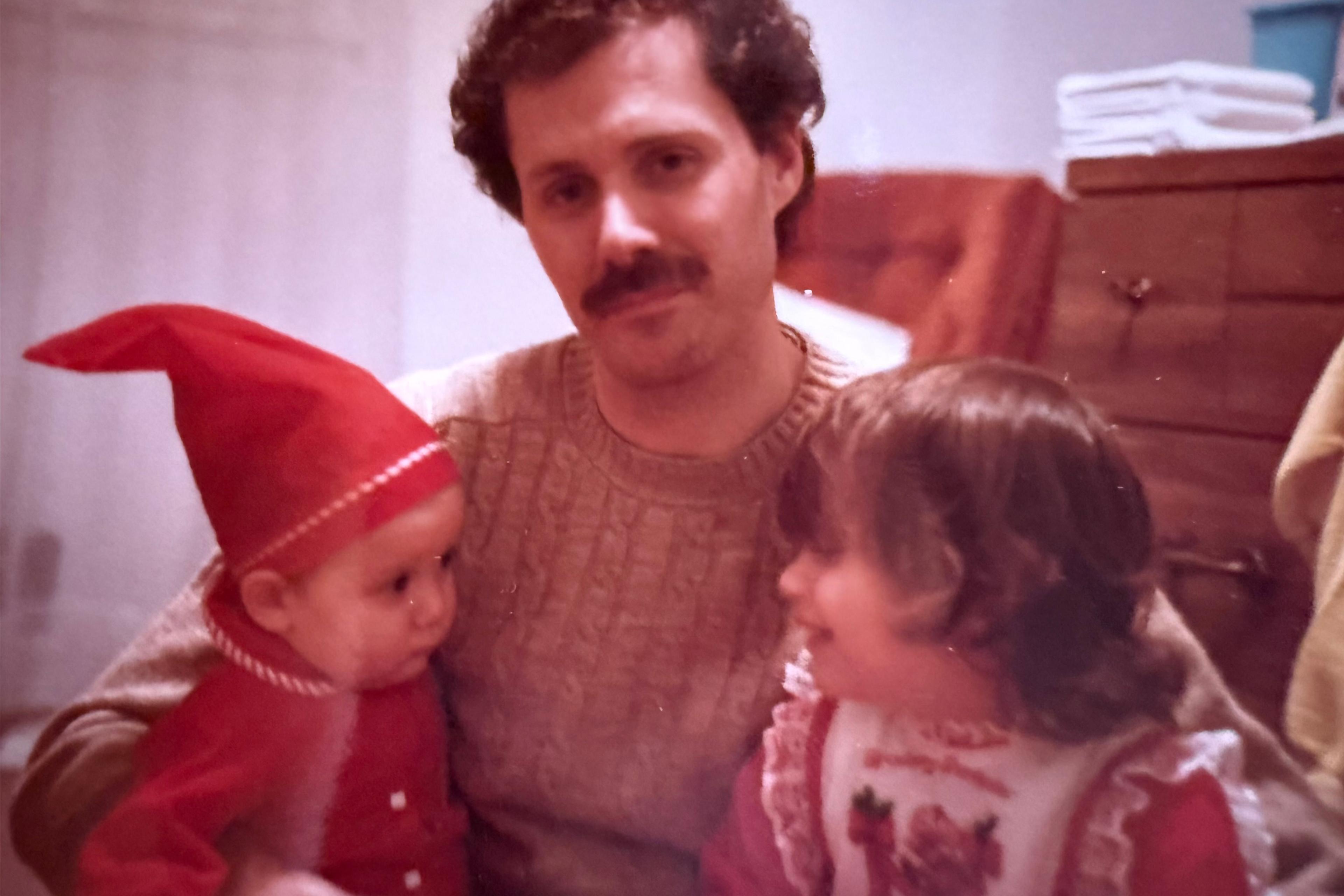 Vintage photo of a man with a moustache holding a baby wearing a red pointed cap and a young child