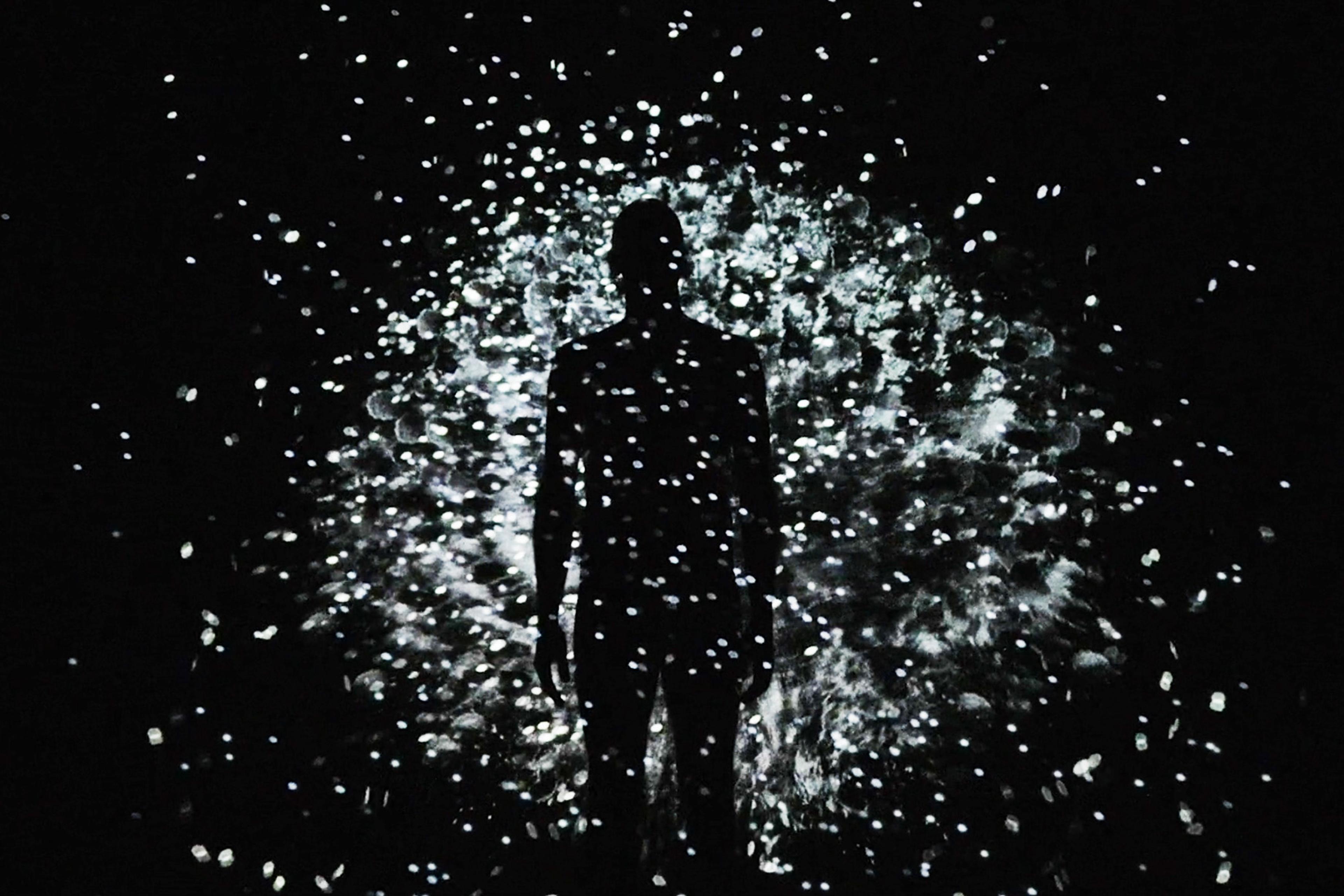 Silhouette of a person surrounded by a burst of white, glowing particles against a dark background.