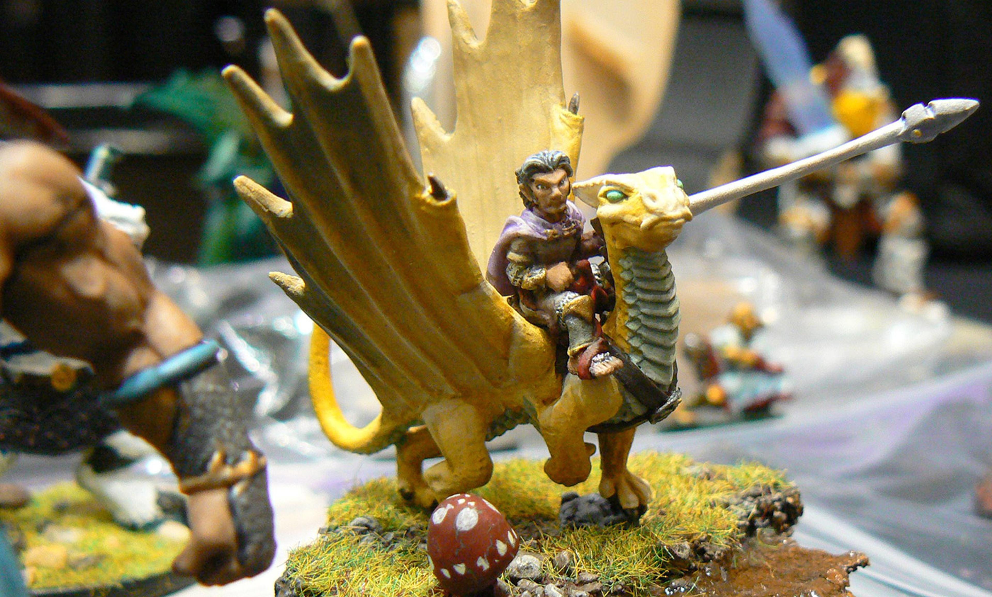 A detailed miniature figure on a winged creature holding a spear on a grassy base with a red mushroom in the foreground.