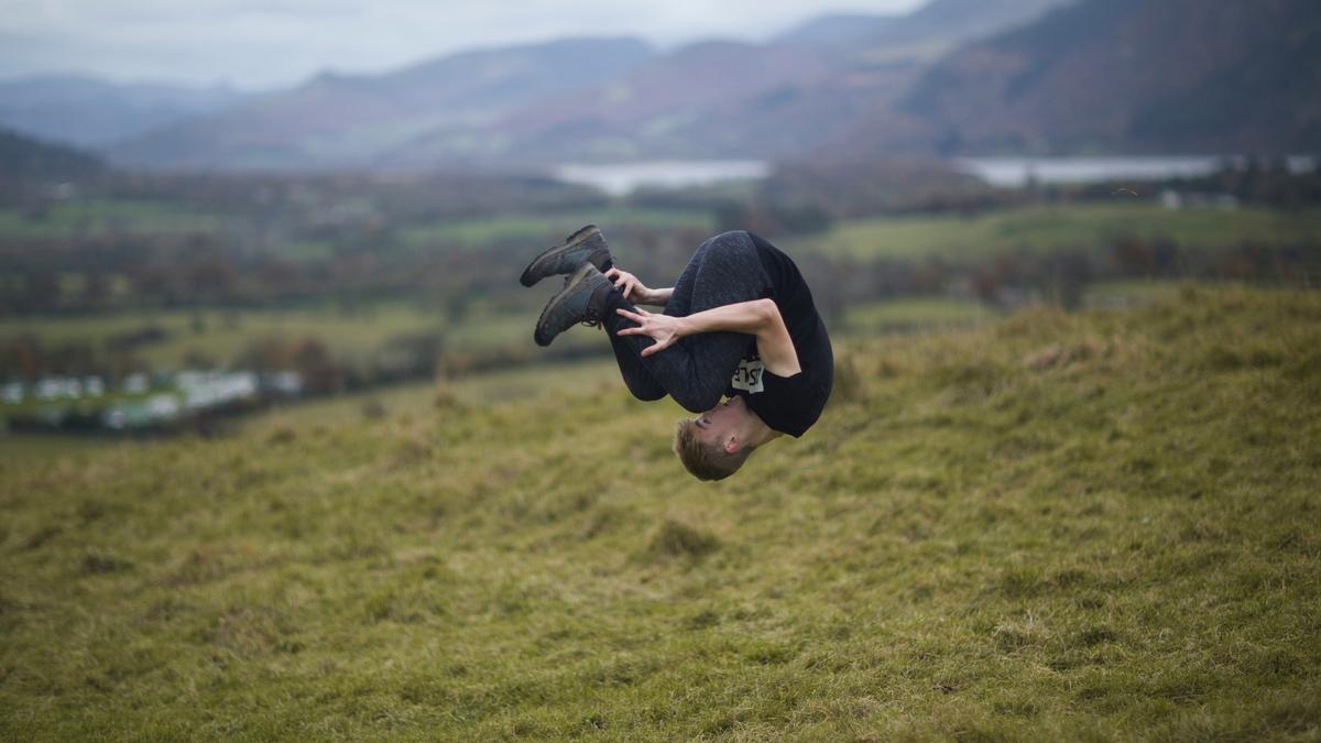 A person in the air, mid-flip, on a grassy hill with distant hills in the background.