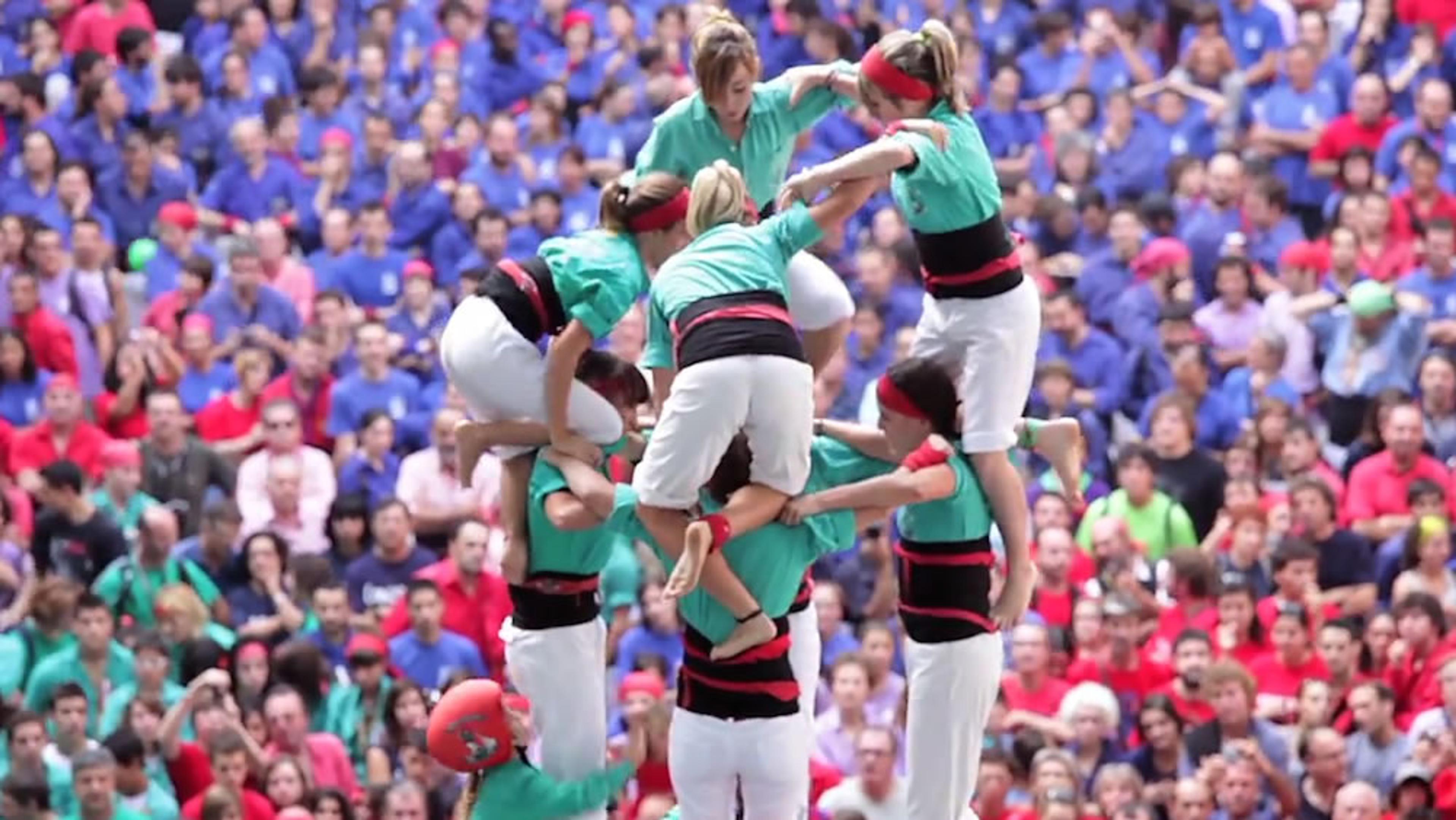 A human tower formation with a large crowd in colourful clothing in the background, focusing on the participants’ coordination.