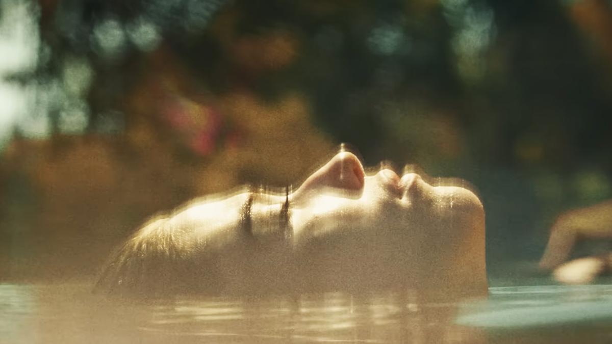 Photo of a woman floating on their back in water with sunlight on their face and blurred foliage in the background.