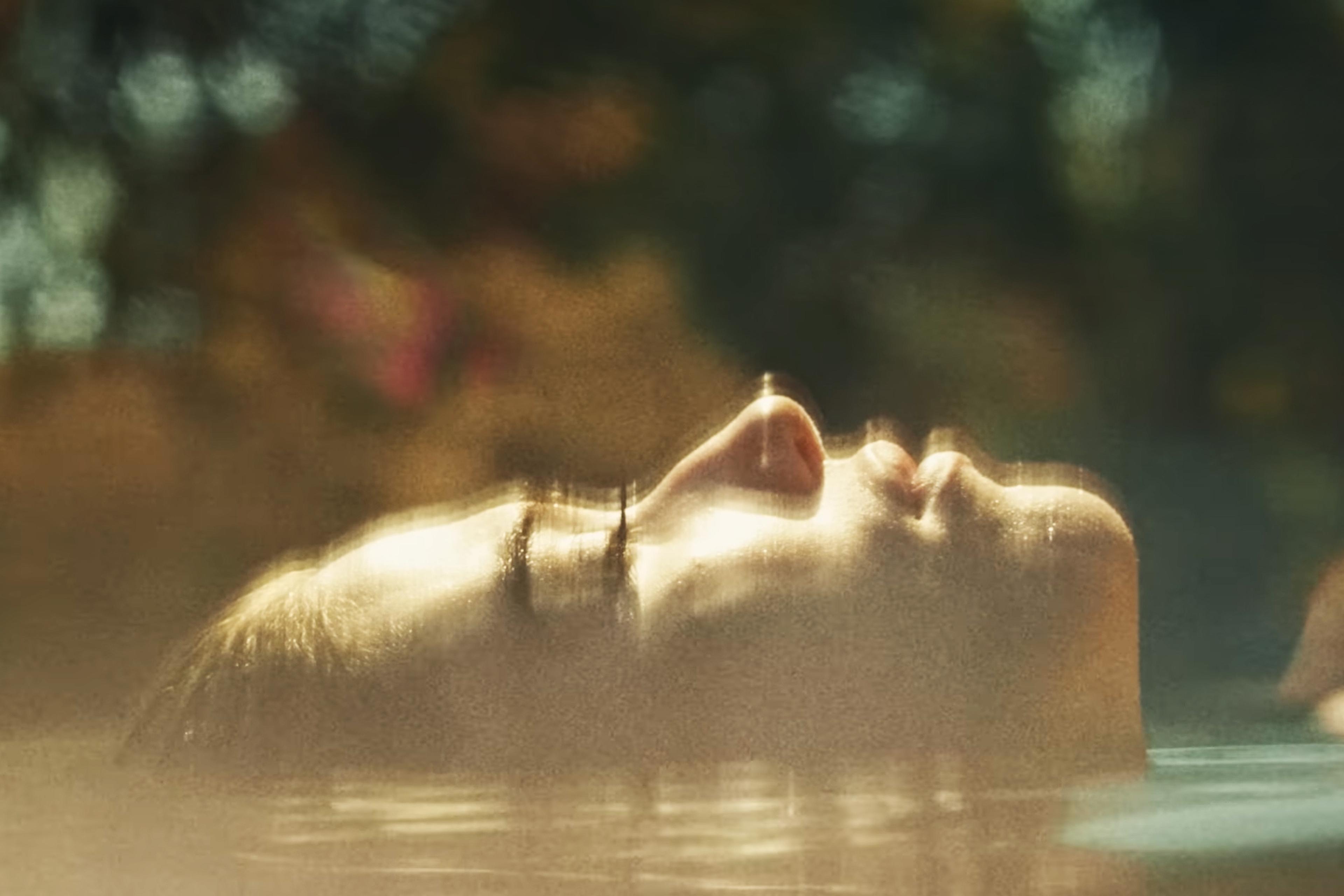 Photo of a woman floating on their back in water with sunlight on their face and blurred foliage in the background.