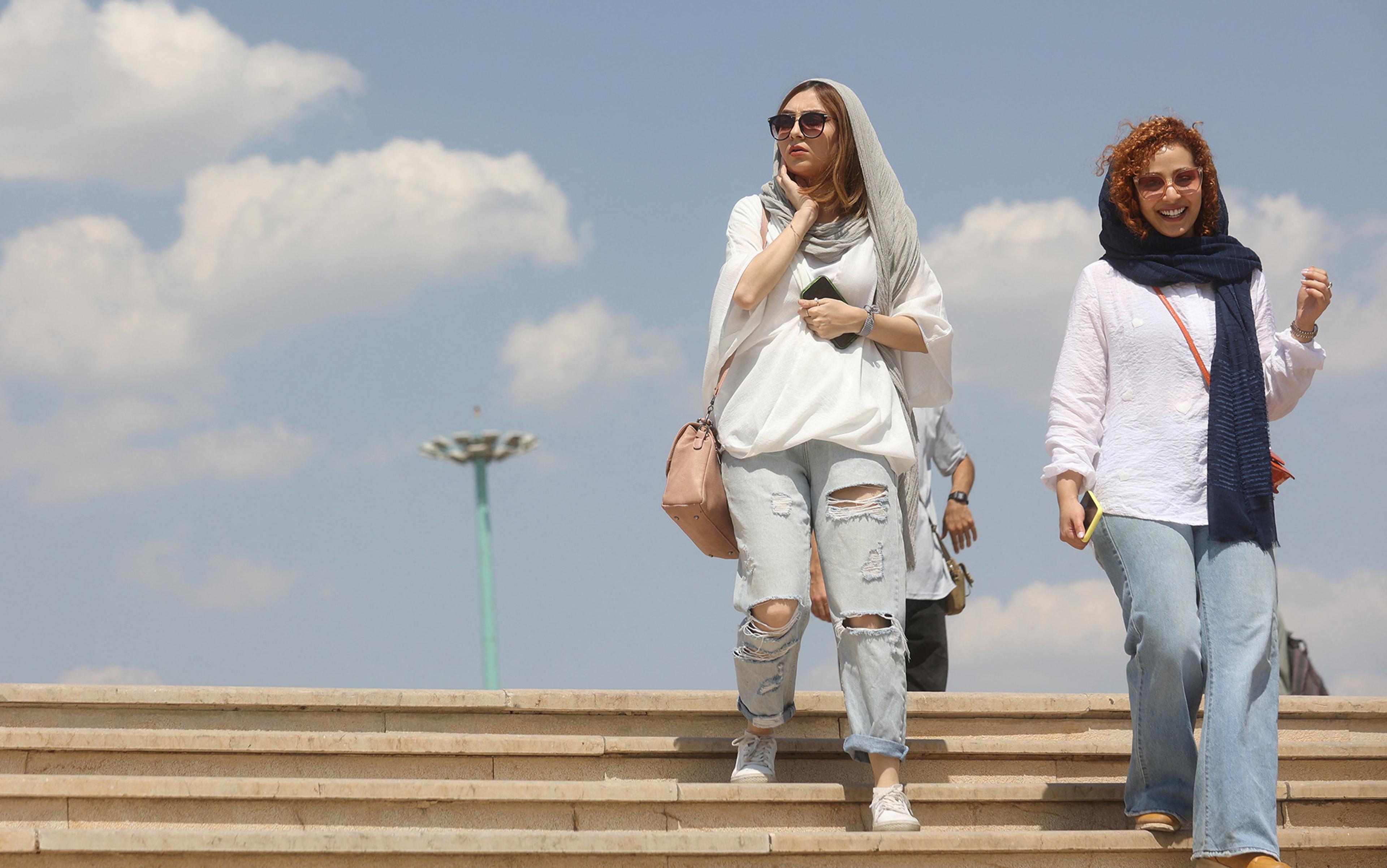 Two fashionably dressed women in modern style hijabs descend steps beneath a blue sky