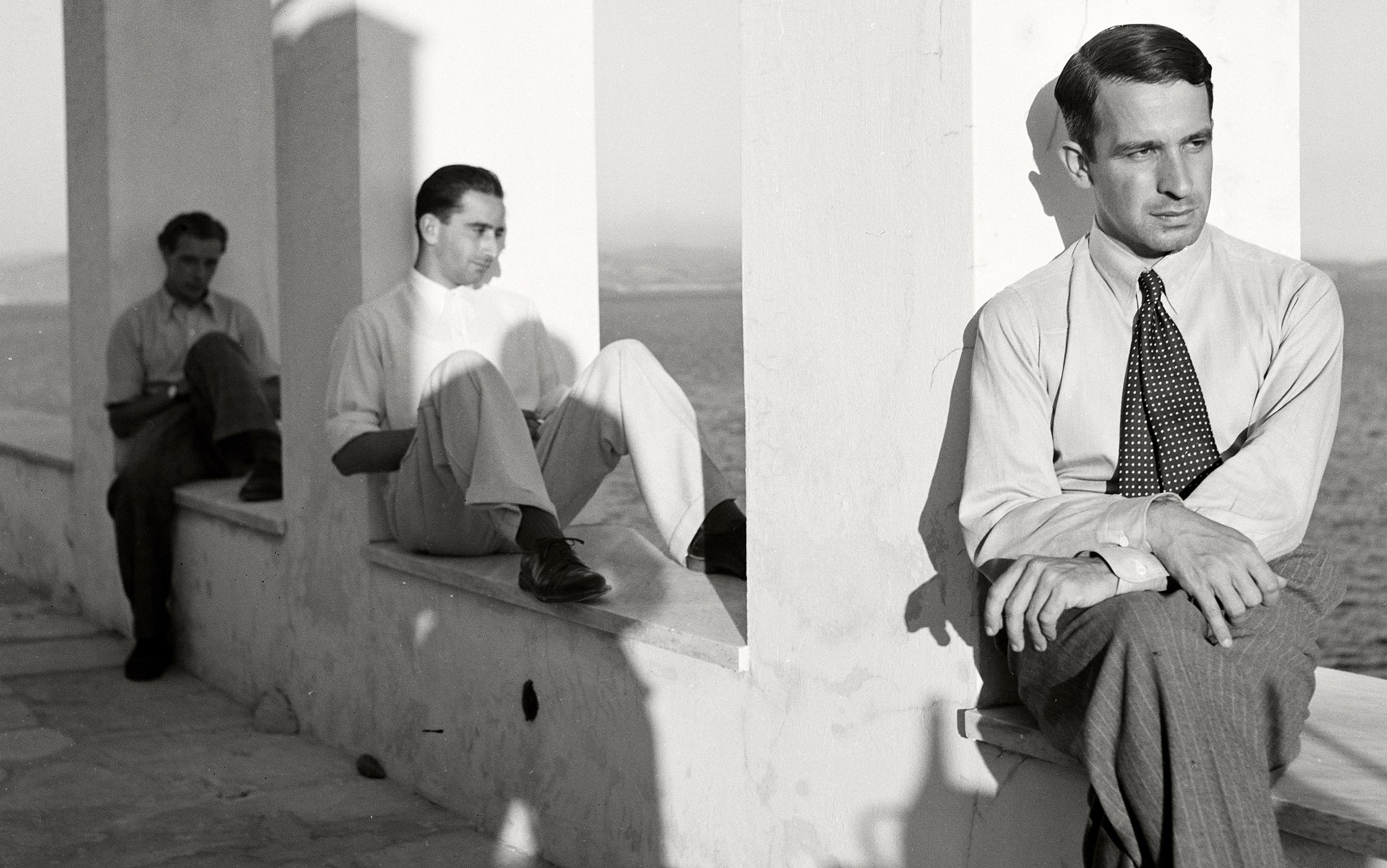 A black and white shot shows three men sitting on a sea wall and seen from a diminishing perspective such that they represent a scale of size