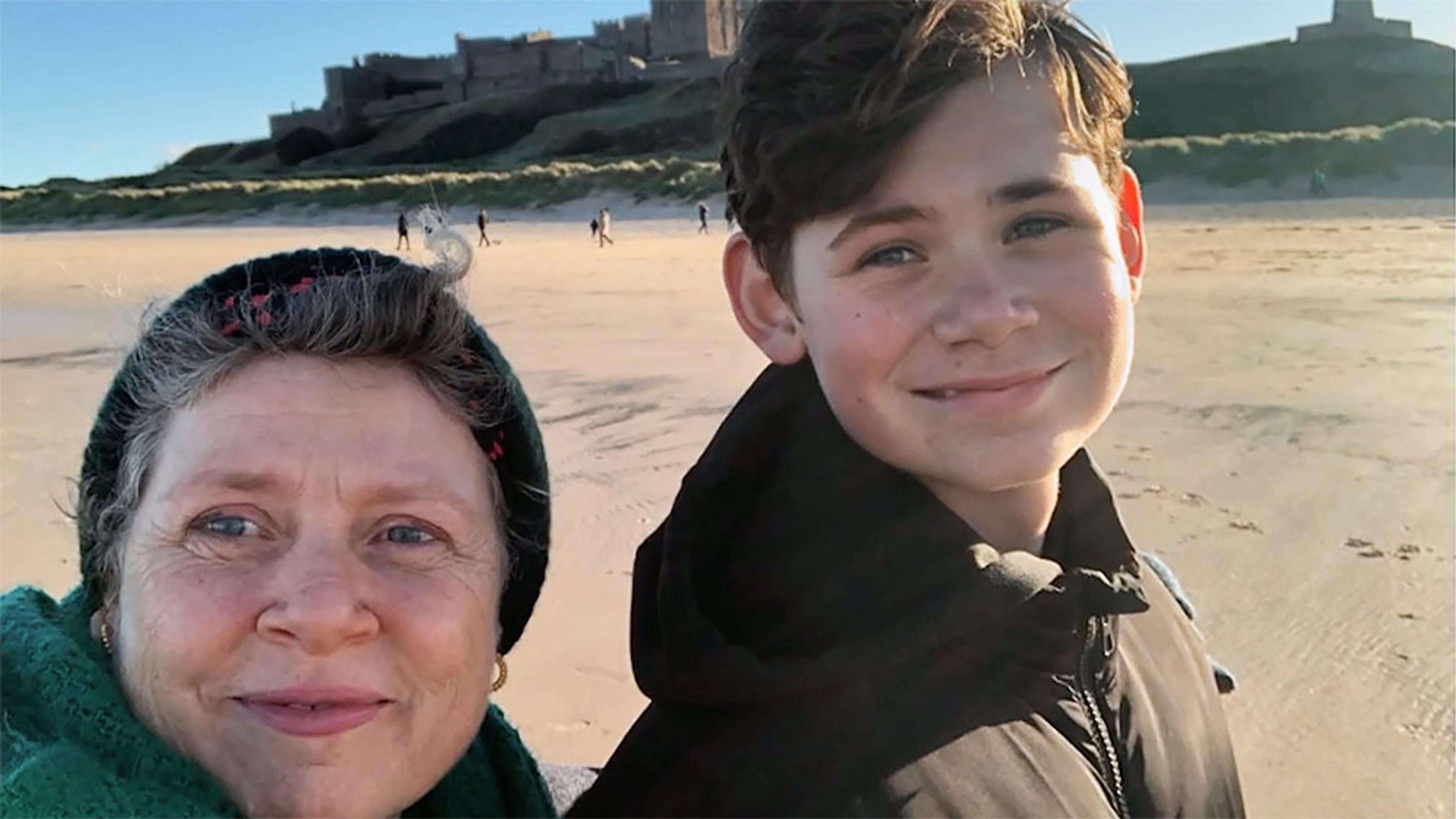 Selfie of a woman and boy smiling on a sandy beach with a castle in the background on a sunny day.