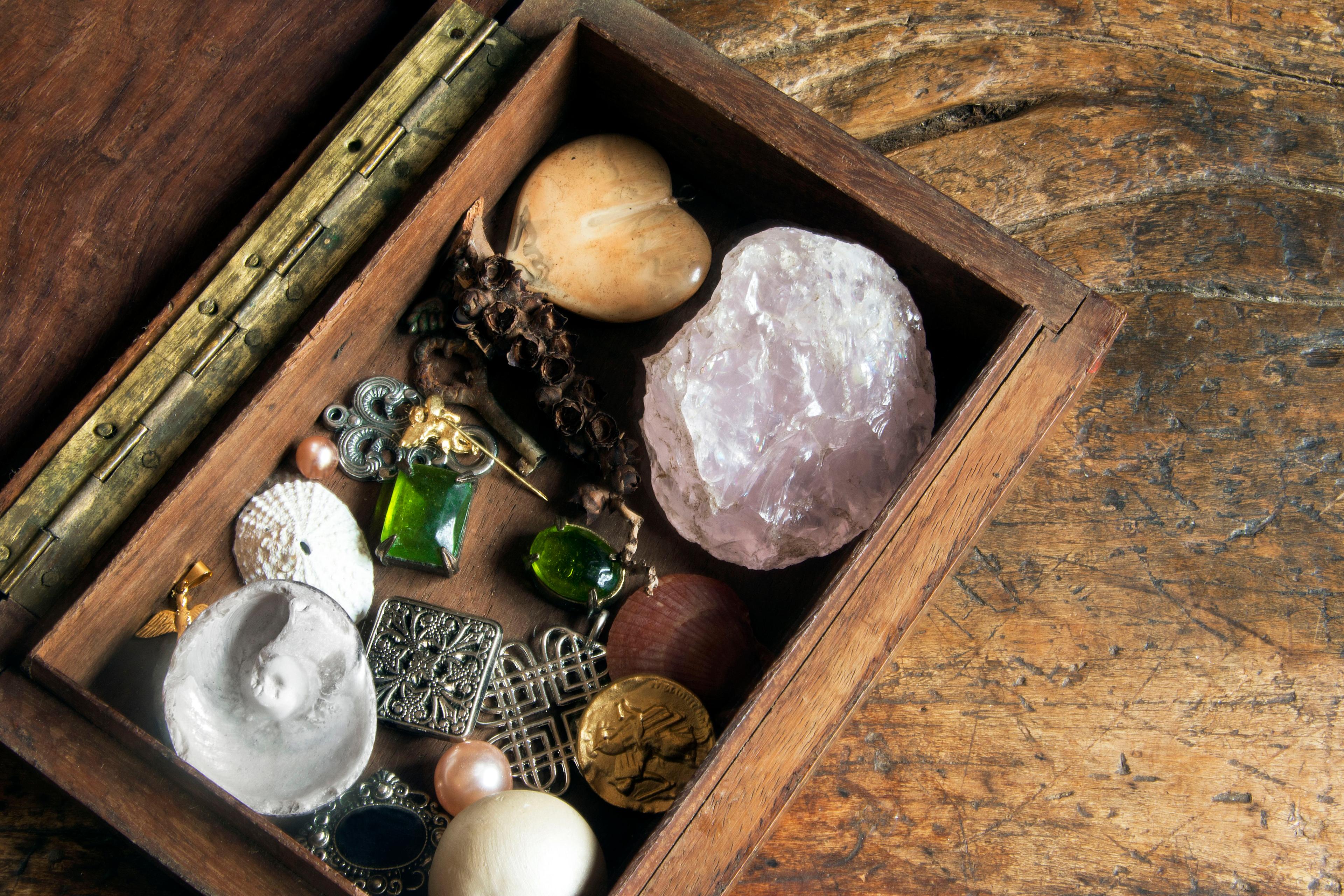 Photo of an open wooden box with various trinkets including stones, jewellery and shells on a rustic wooden surface.
