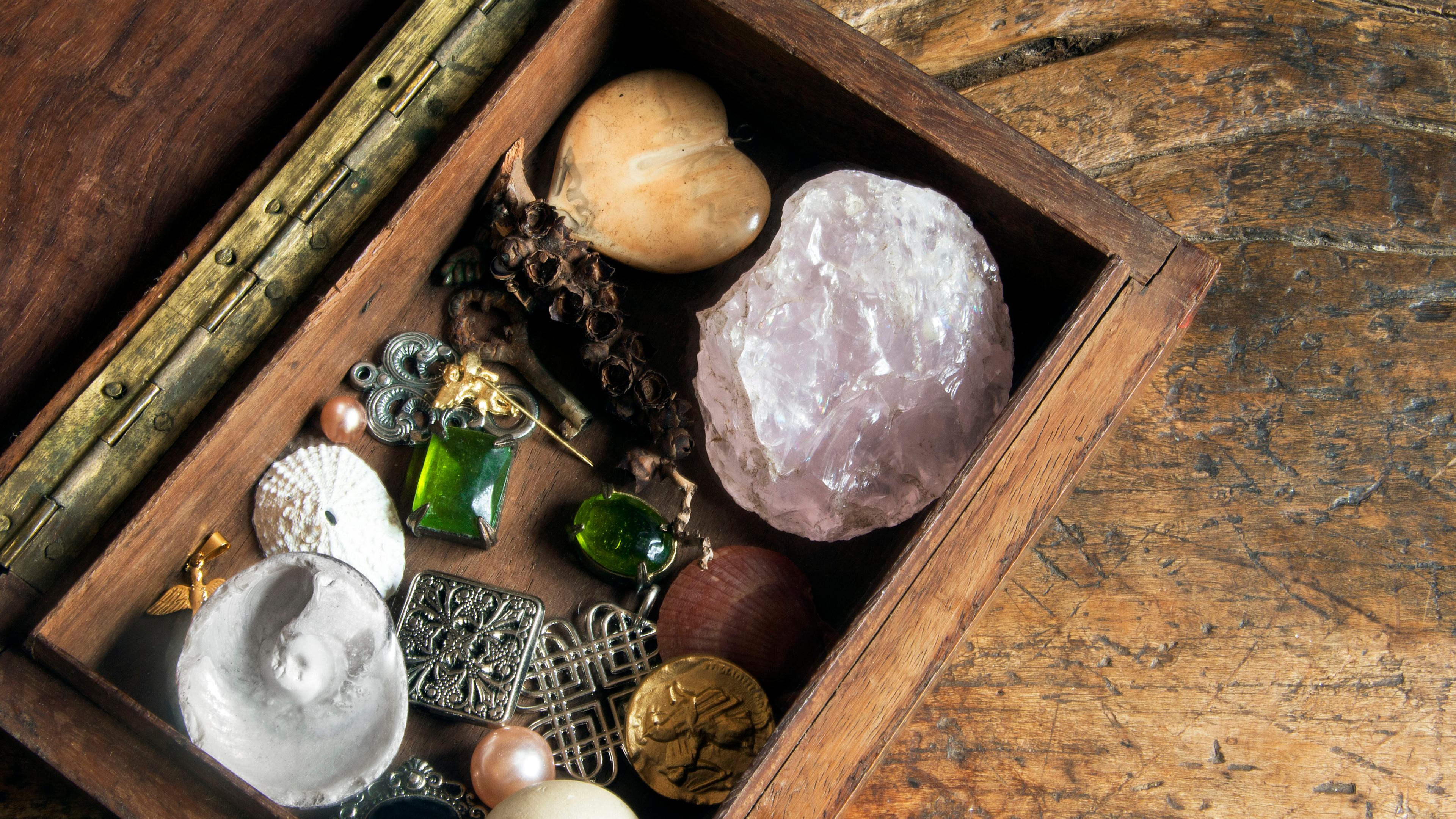 Photo of an open wooden box with various trinkets including stones, jewellery and shells on a rustic wooden surface.