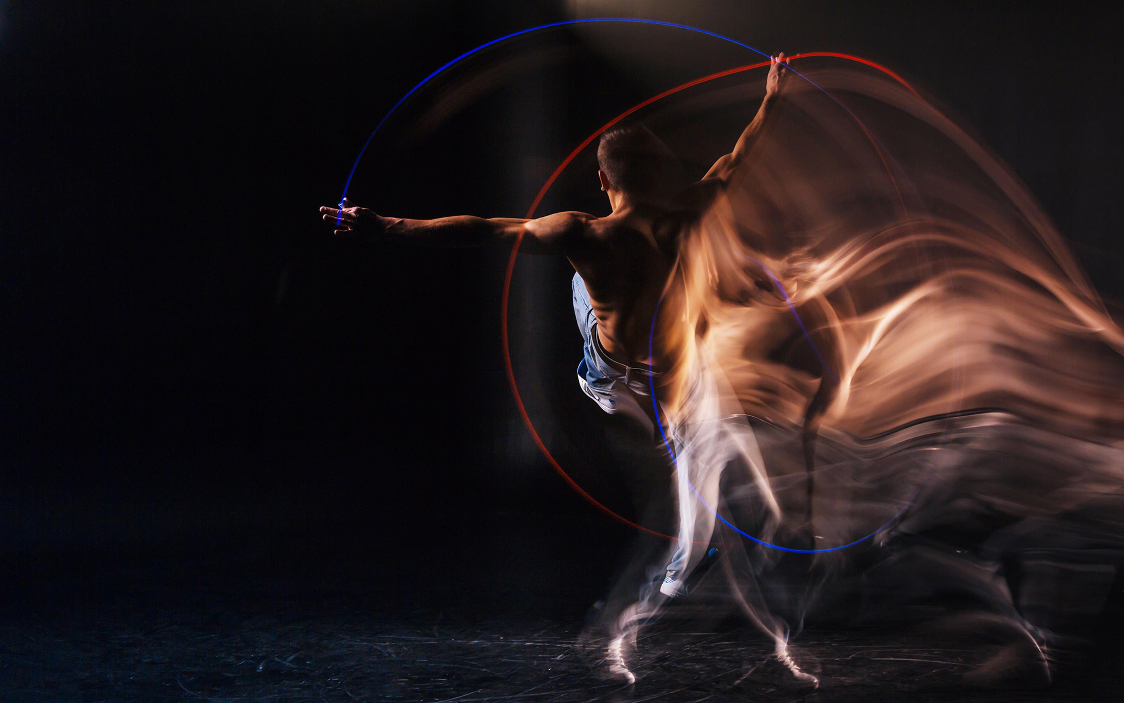 A double-exposure image of a dancer on stage against a black backdrop, his body is lit and partly shot in motion blur