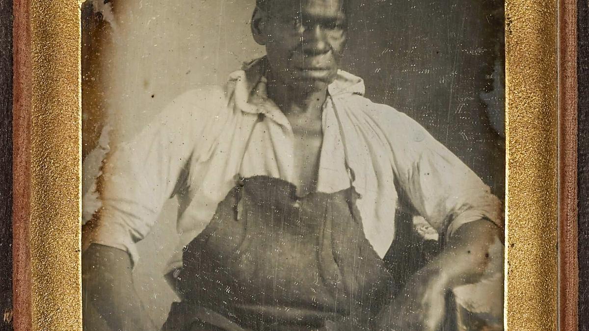Daguerreotype of a seated man wearing an apron and a partially open shirt framed in a gold mat.