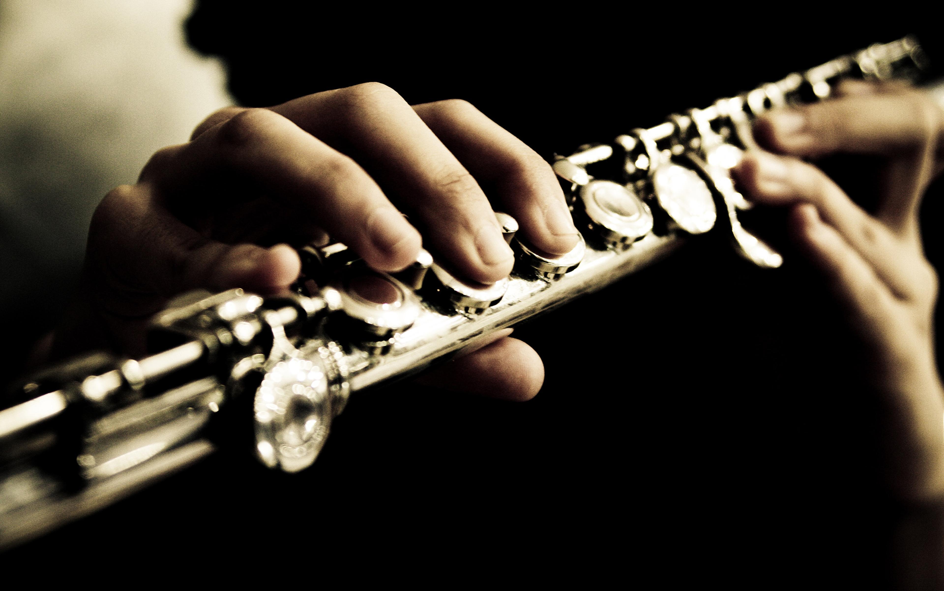 A close up picture of hands playing a silver brass flute with a shallow depth of field such that the foreground fingers and keys are more in focus