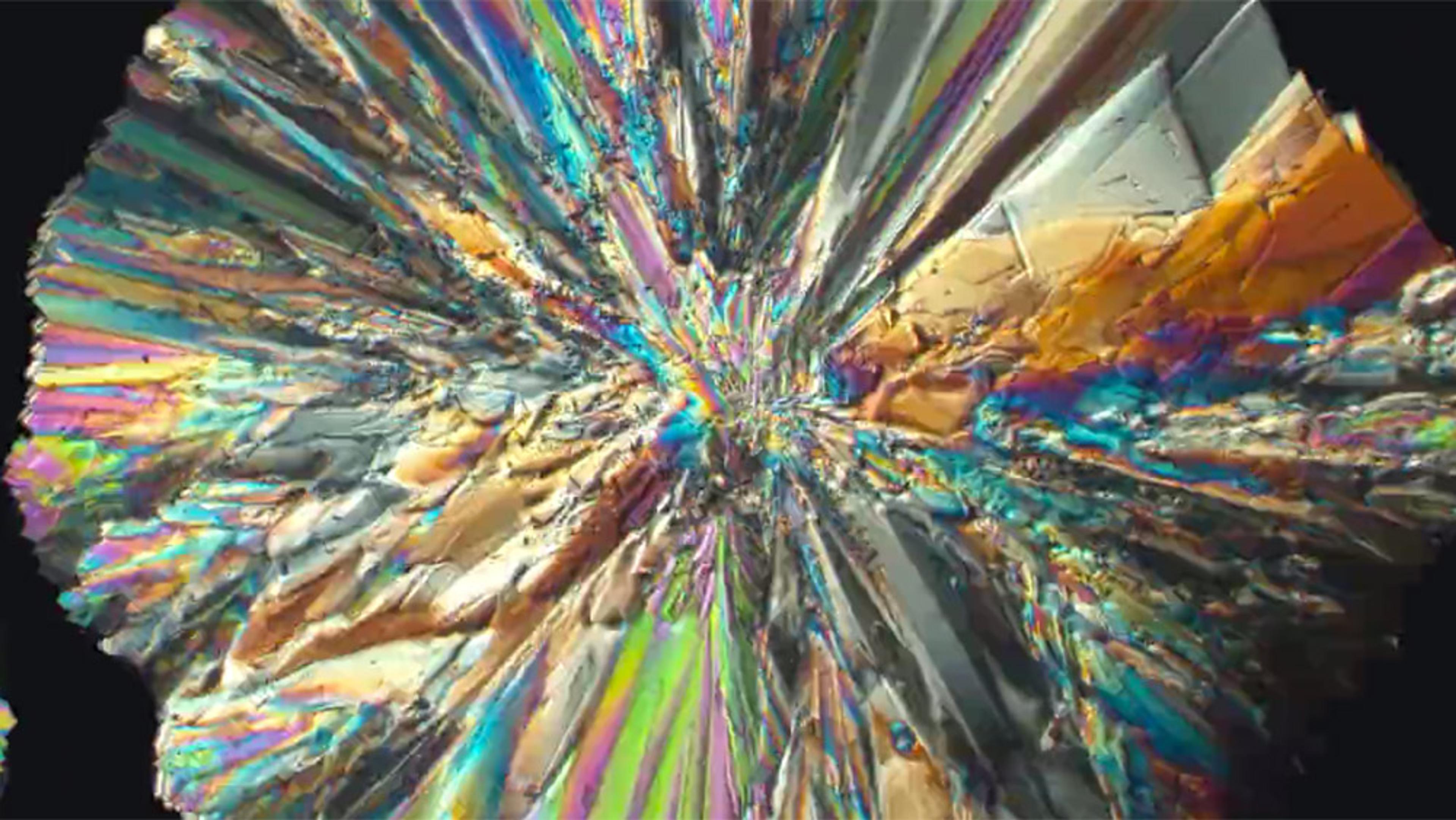 Close-up photo of vibrant and multicoloured crystalline structures radiating from the centre, resembling a kaleidoscope pattern.