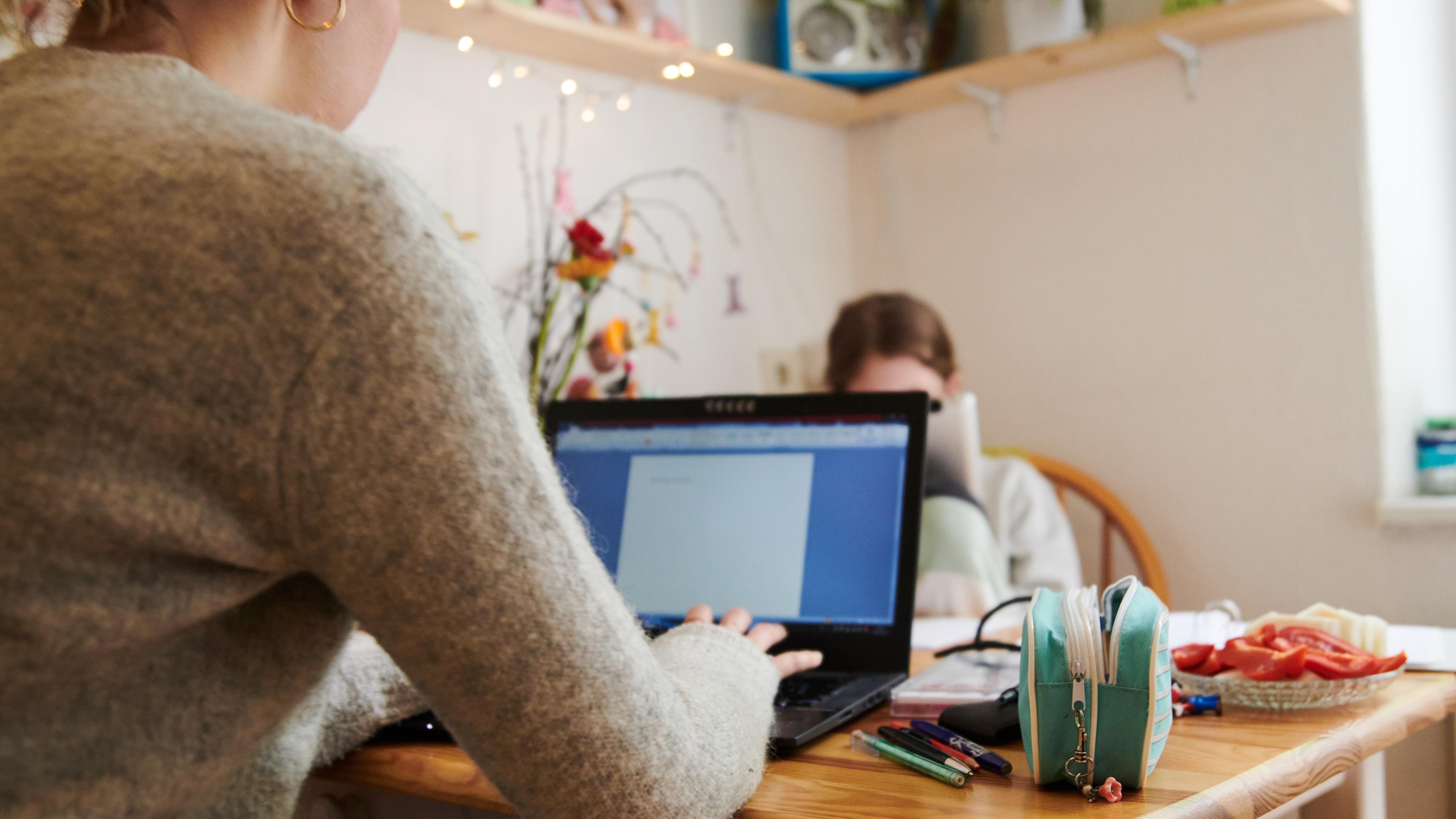 Photo of a person using a laptop on a wooden table with stationery books and a plate of snacks also visible.