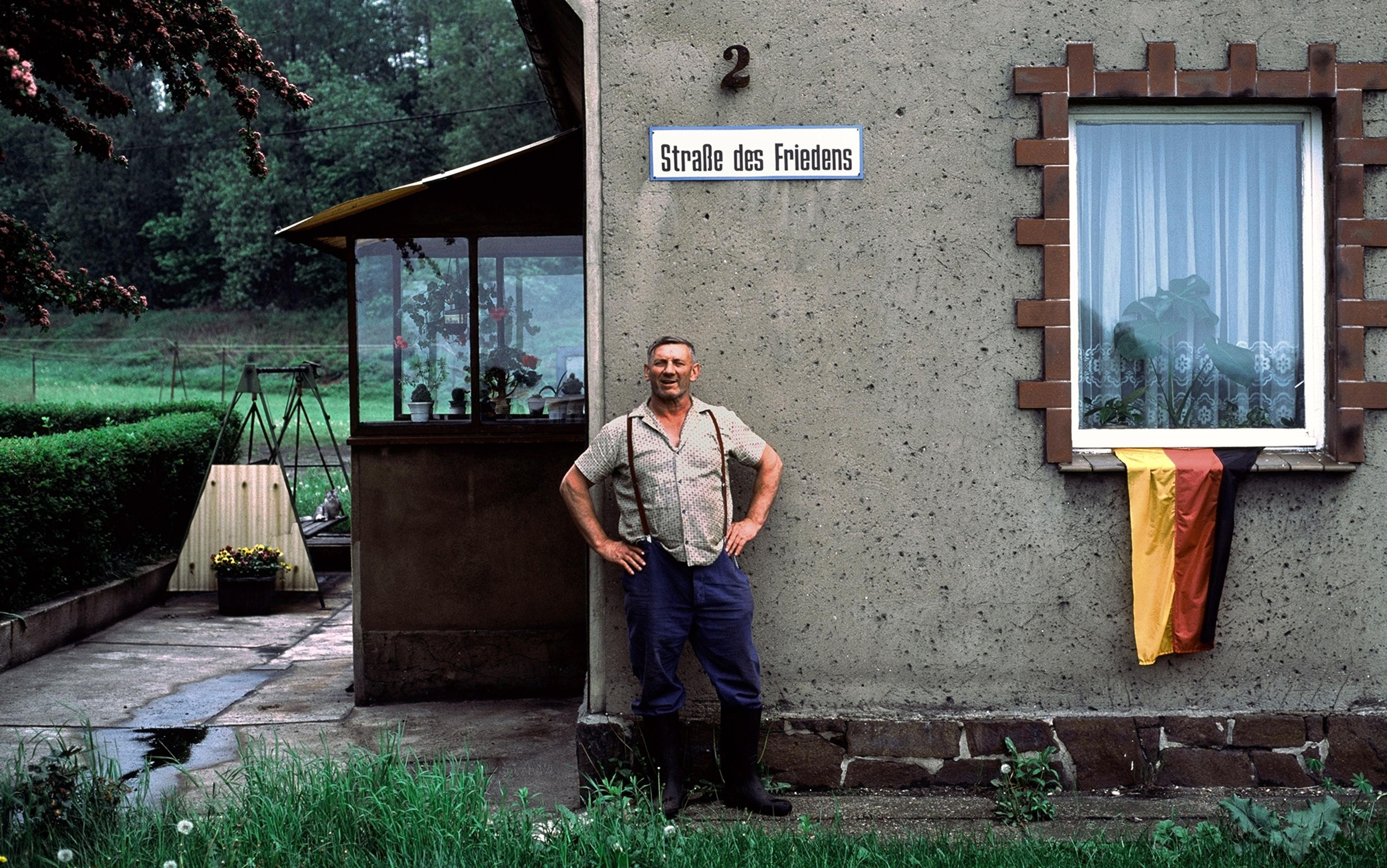 An older man stands proudly in front of his house near Leipzig, east Germany after reunification in 1990. A German flag hangs from a ground floor window.