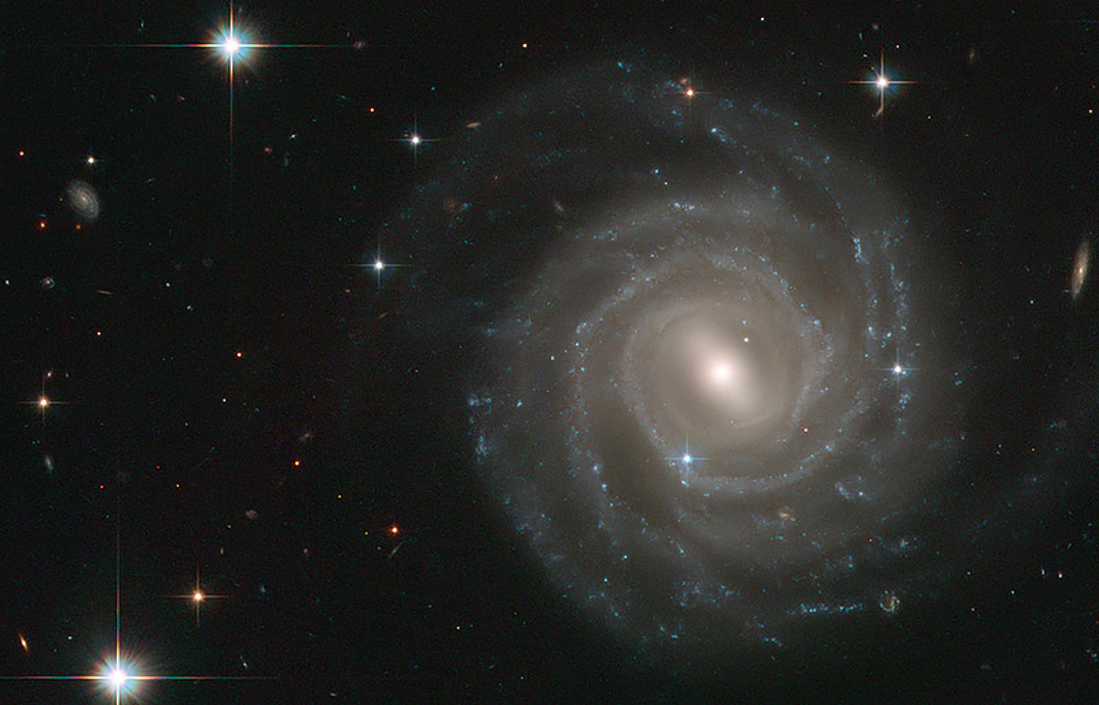 A spiral galaxy with bright stars on the edges and in the background, against a dark space backdrop.