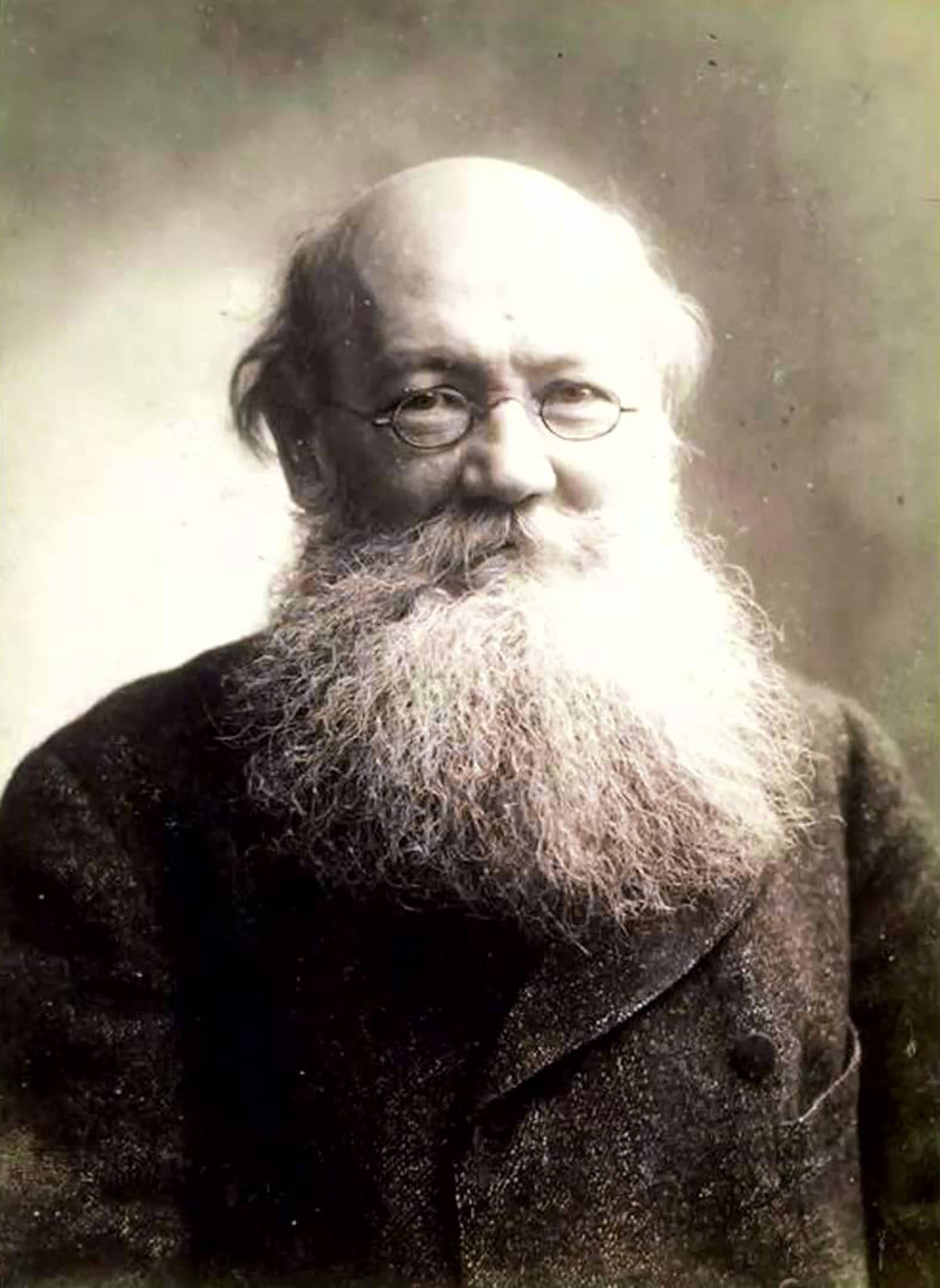 Black-and-white photo of an elderly man with glasses and a long white beard. He is wearing a dark, heavy coat and looking at the camera.
