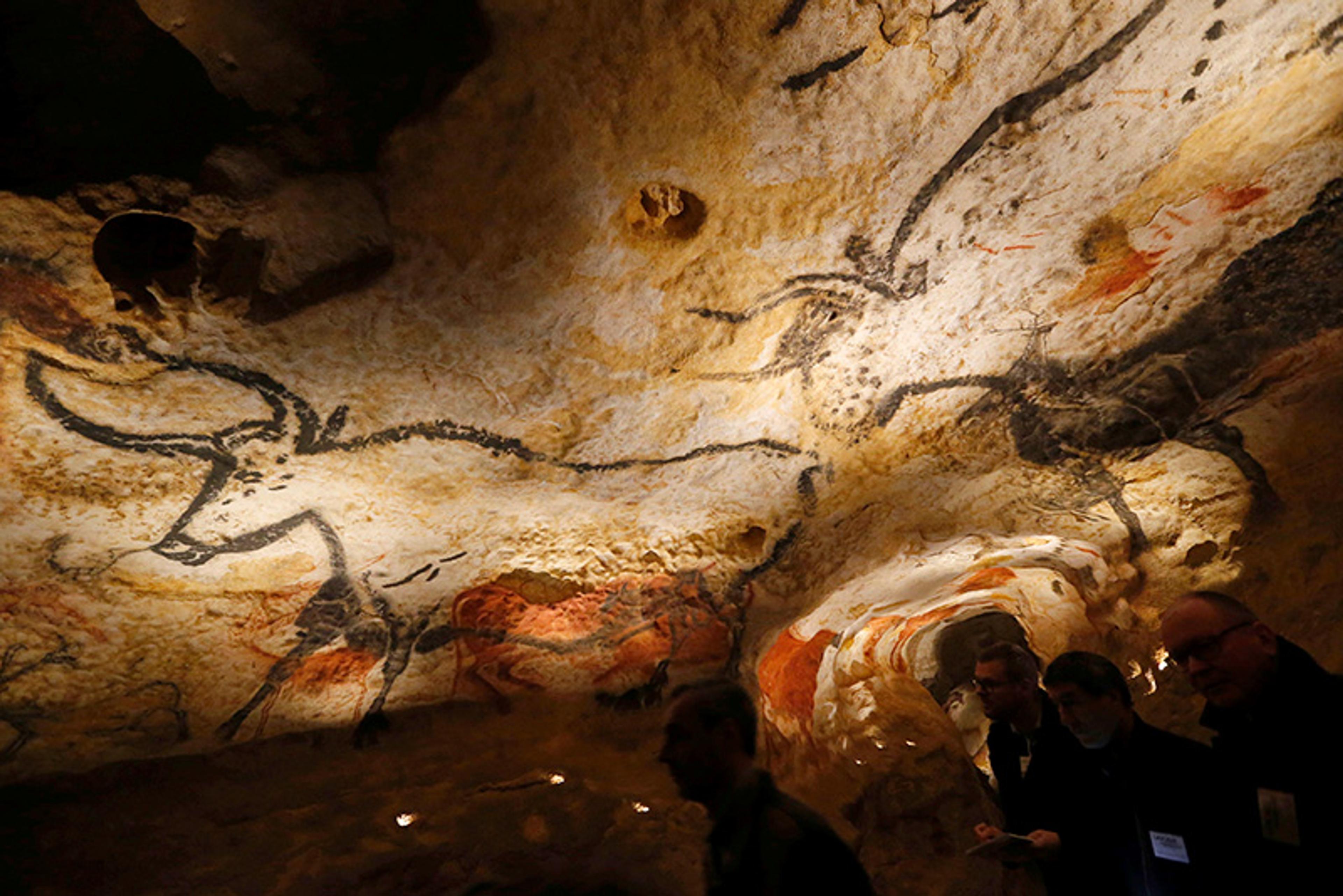 Prehistoric cave paintings showing animals on a rough, uneven ceiling with people observing them from below.