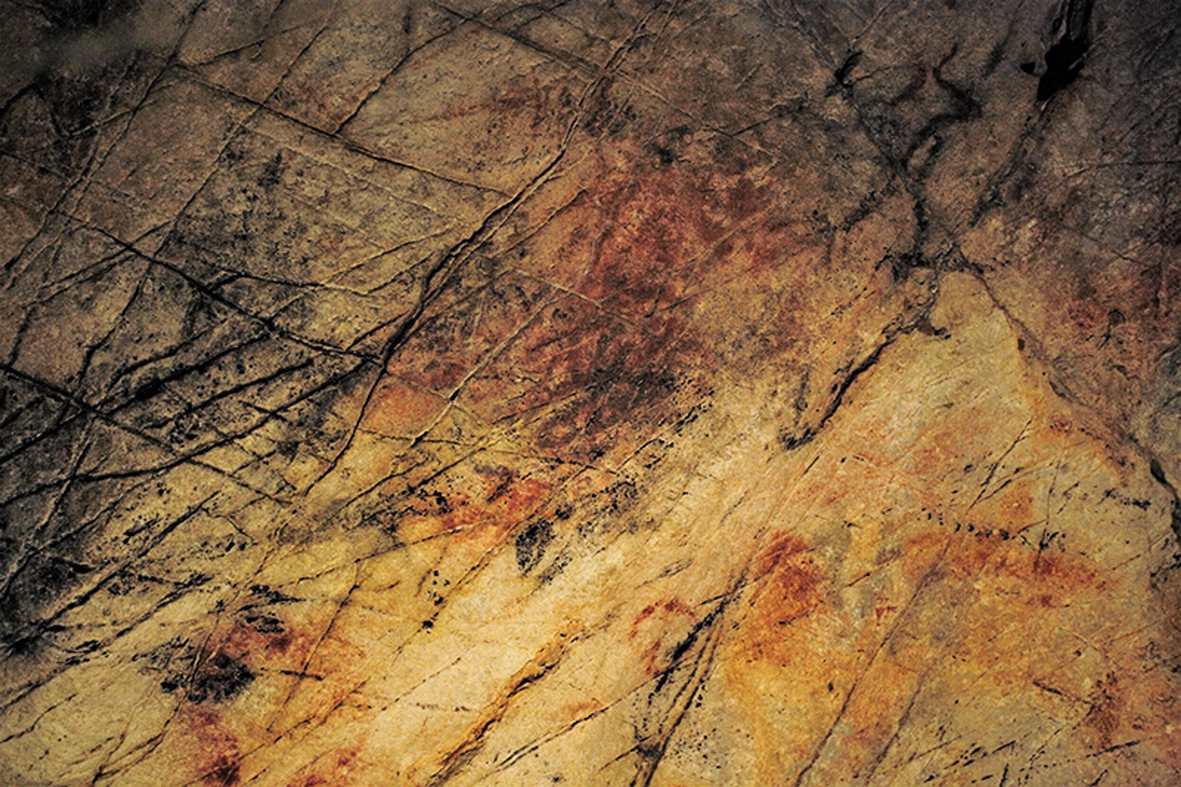 Prehistoric cave art with ochre and charcoal markings on a rough stone surface showing abstract patterns and lines.