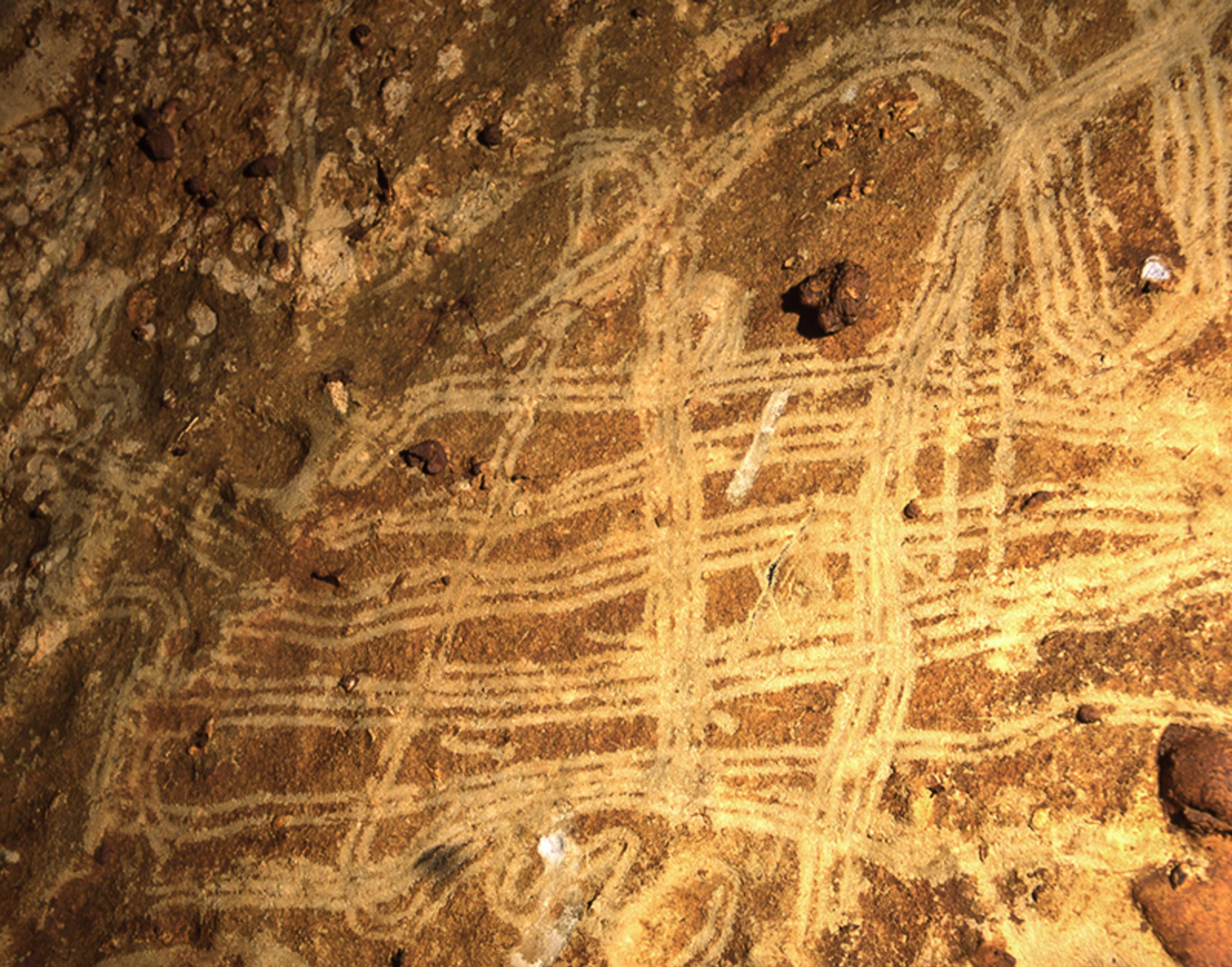 Ancient cave petroglyphs with intricate patterns scratched on a brown rock surface, illuminated by a light source.