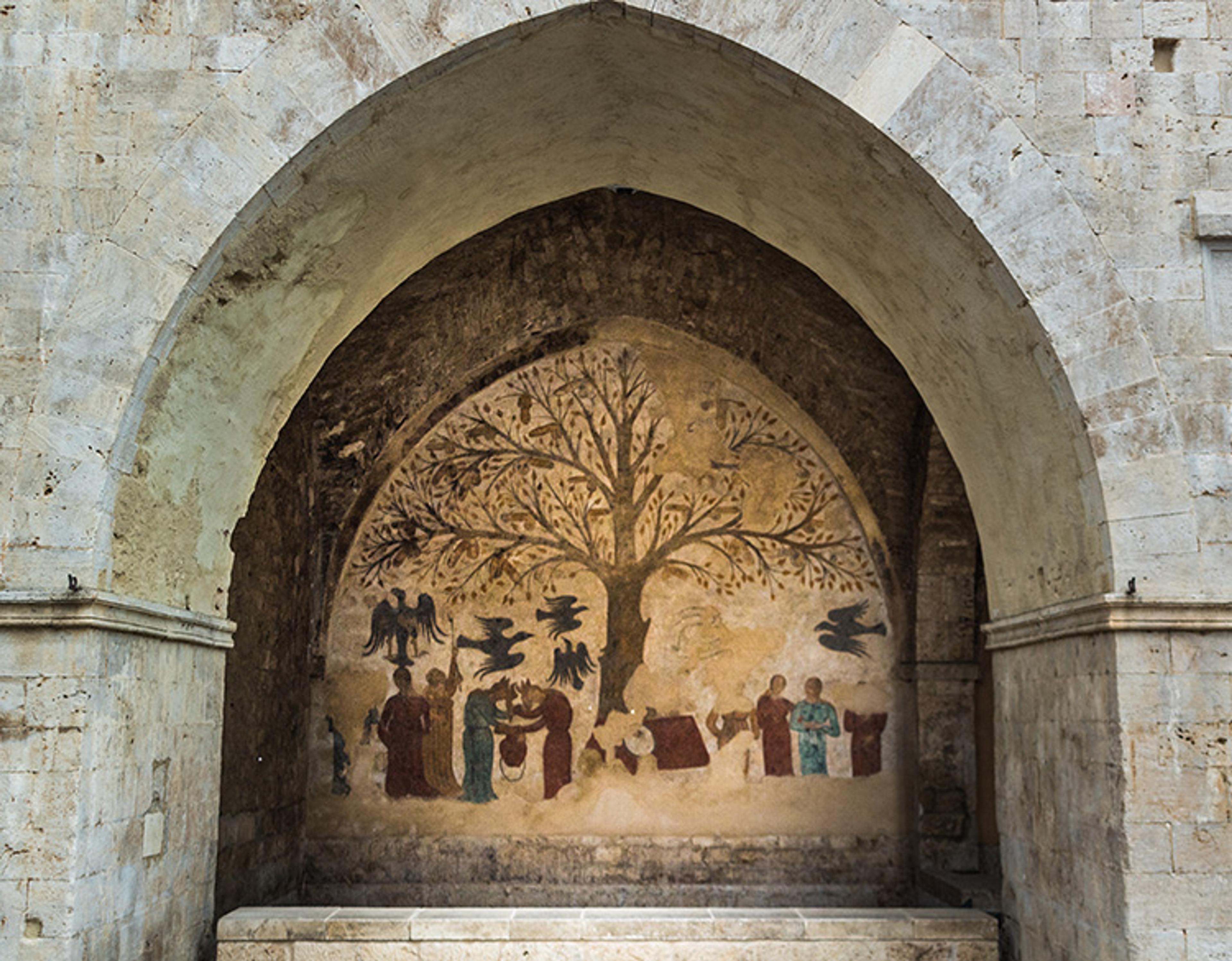 Fresco on a stone archway depicting a large tree with people and birds. The mural is set in the alcove of an aged stone structure.