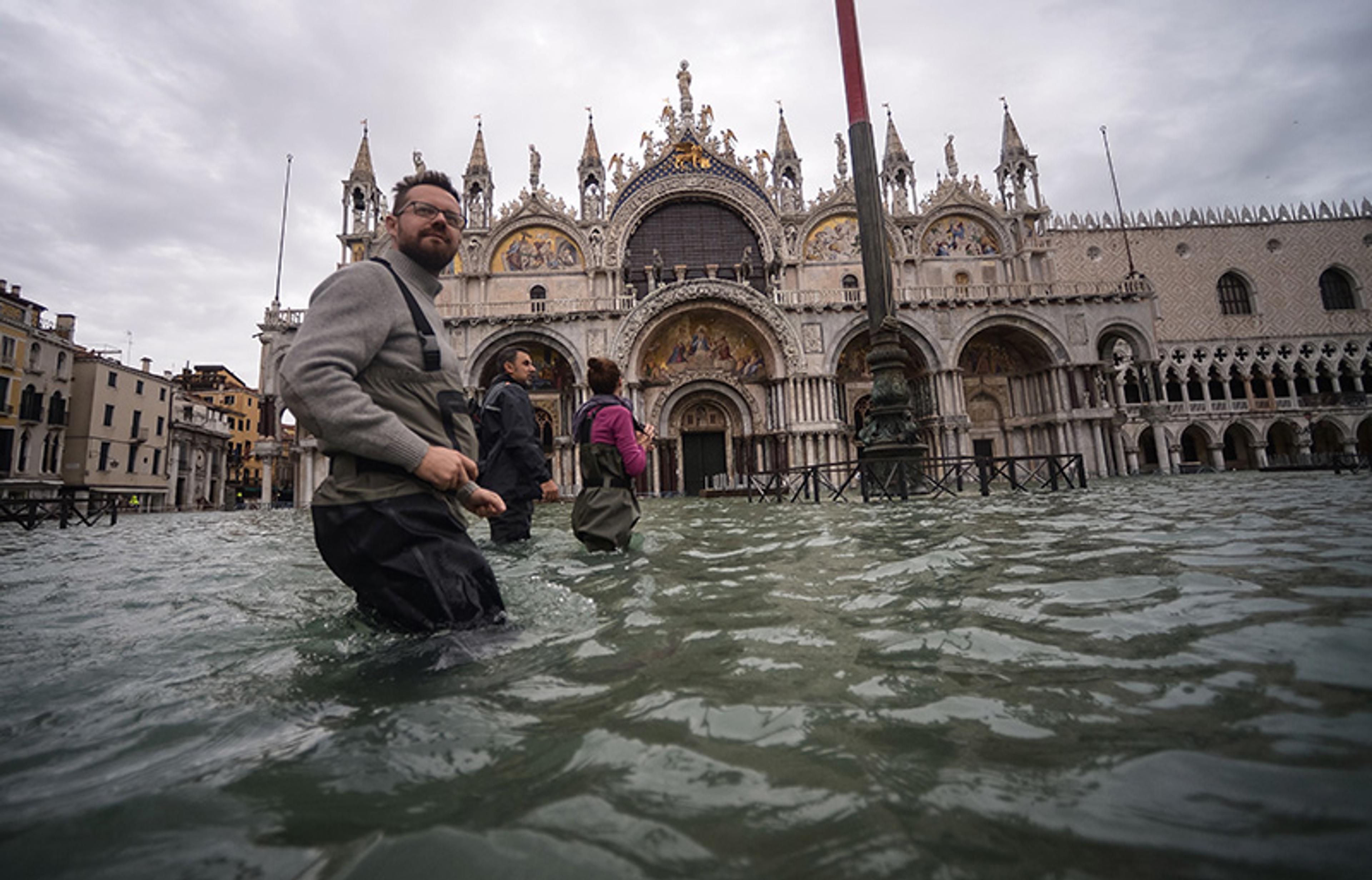People wading through floodwater in front of St Mark’s Basilica in Venice during a cloudy day.