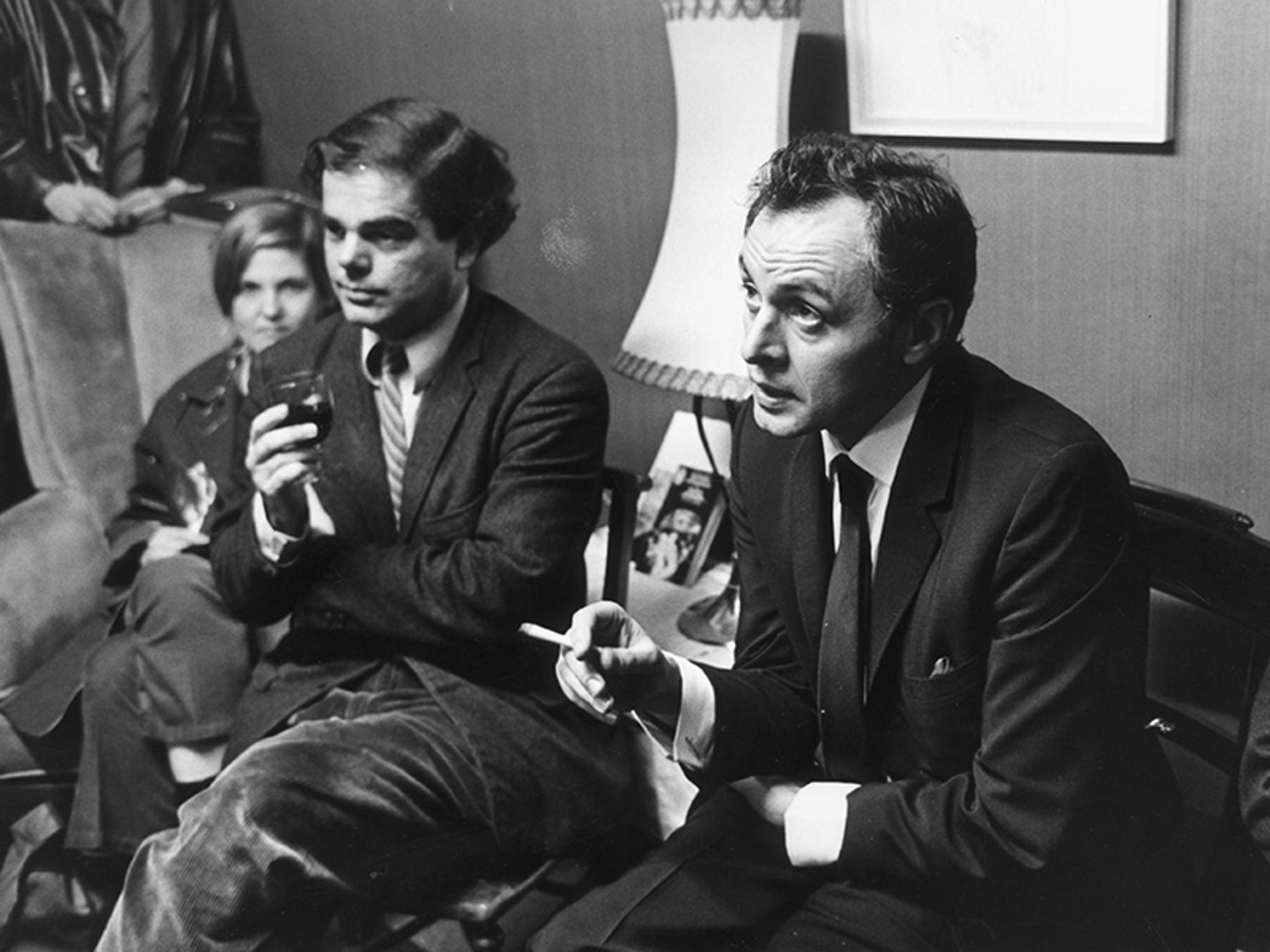 Vintage photograph of three people seated in a room, one holding a drink and another gesturing with a cigarette.